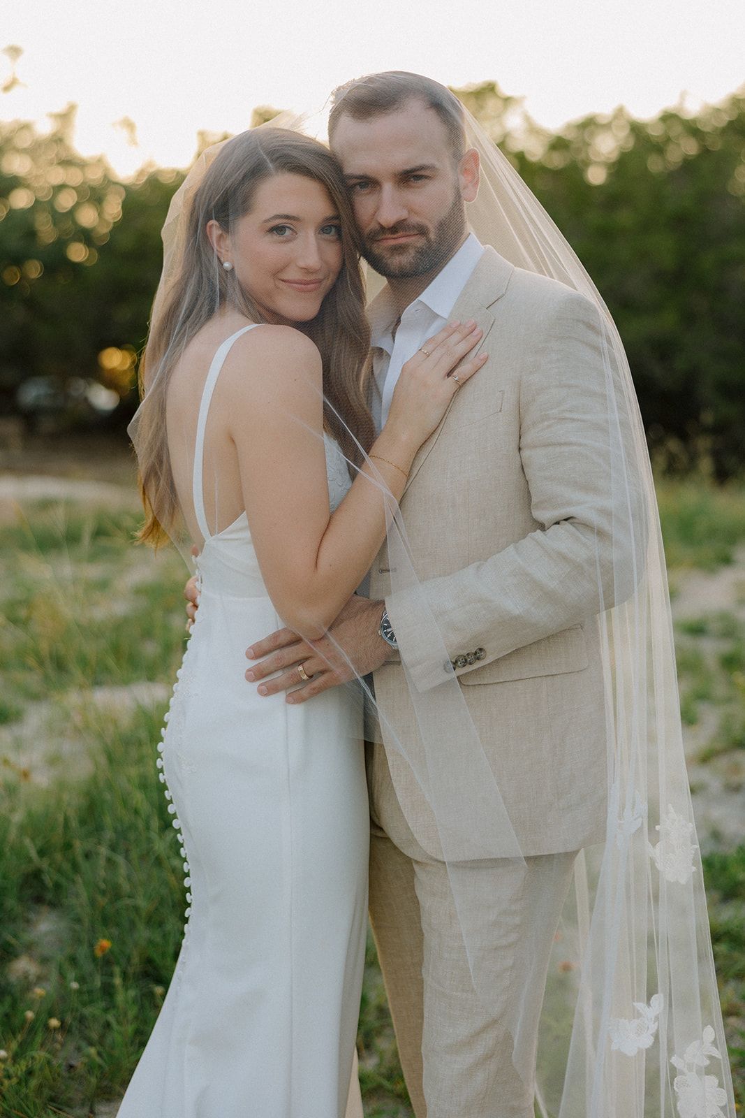 Wedding portrait of newlyweds in elegant white attire during golden hour.