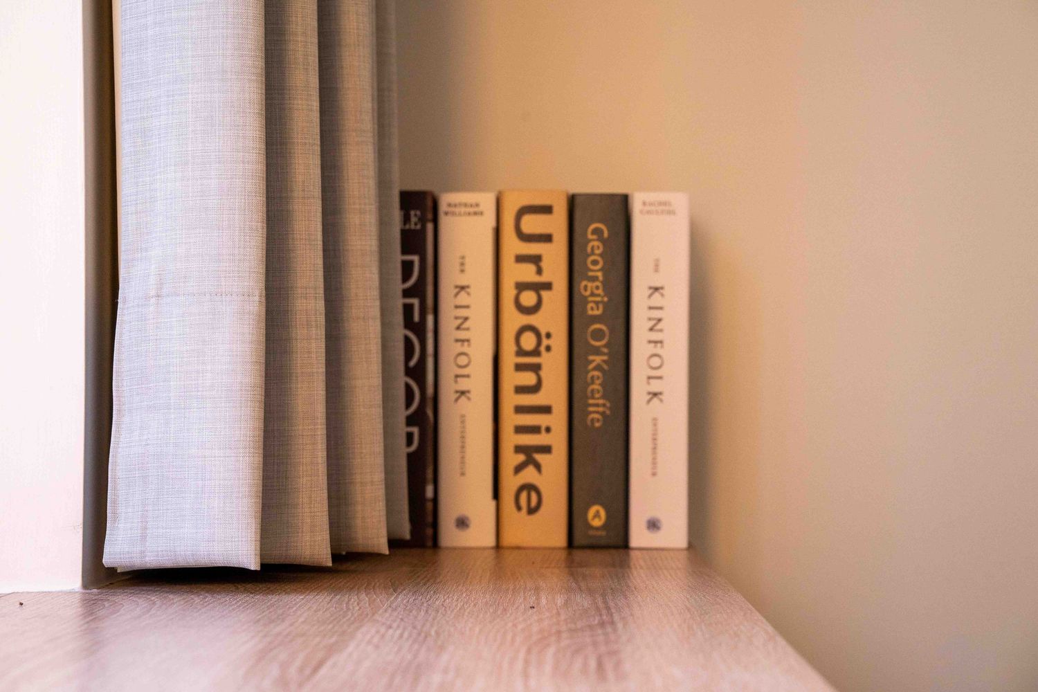 A neat row of black and white books arranged on a wooden shelf against a beige wall with natural lighting.