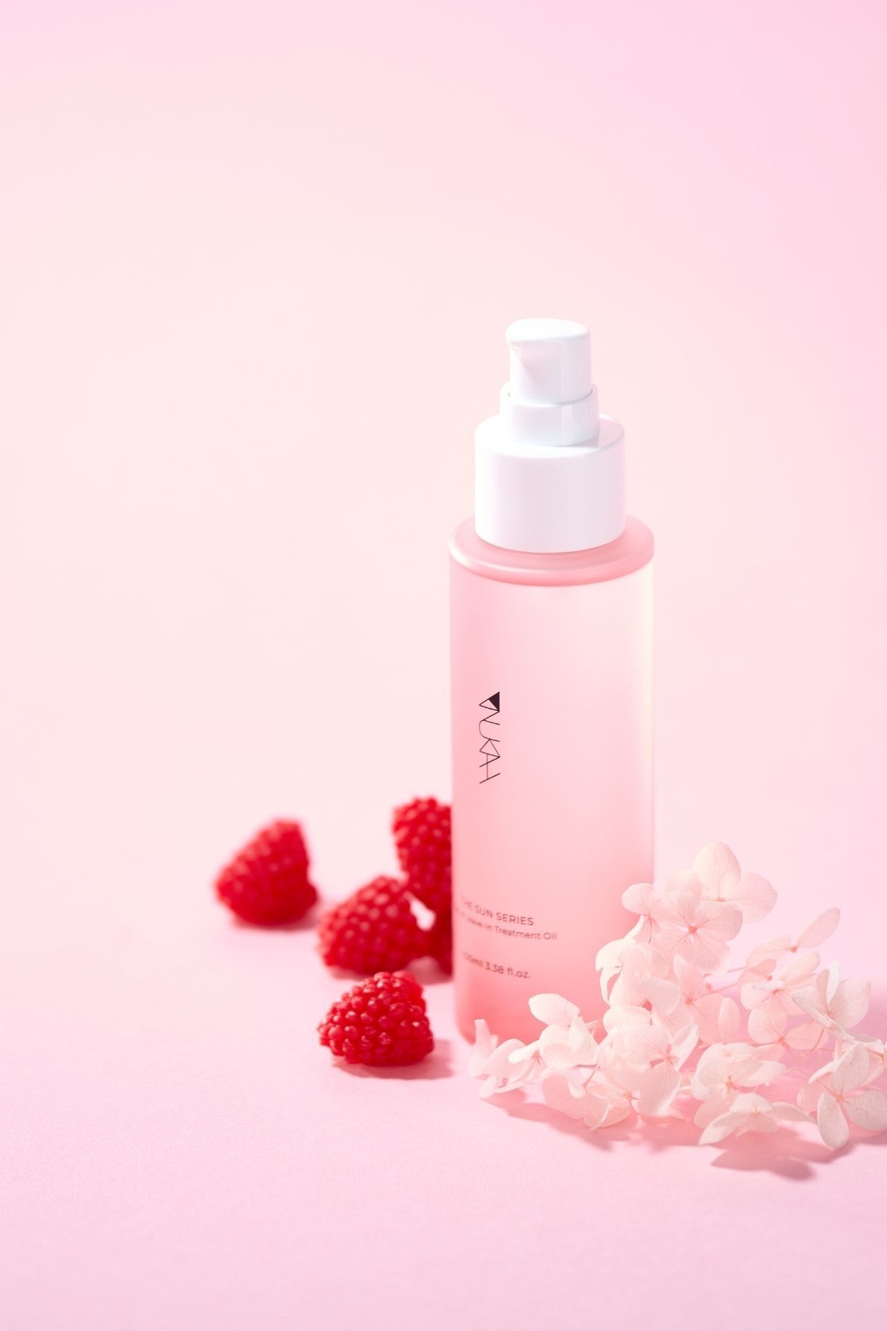 Pink pump bottle serum by VLAA with fresh raspberries and white hydrangea flowers on a soft pink background.