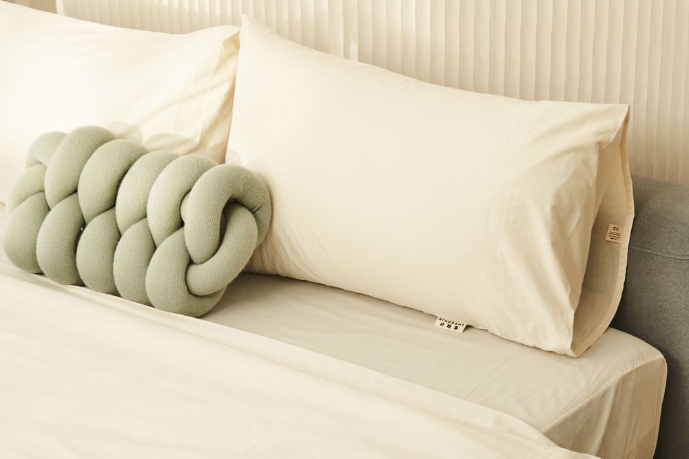 A collection of decorative knotted pillows in neutral beige and sage green colors arranged on a white surface.