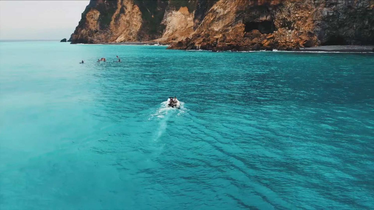 Aerial view of turquoise ocean waters meeting rugged coastal cliffs with waves crashing against rocky shores.