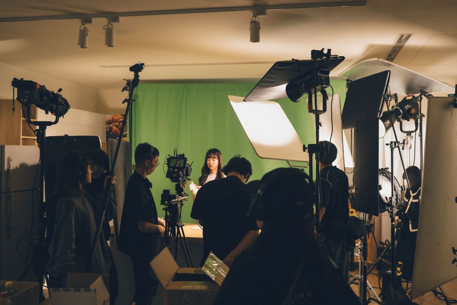 Film crew shooting a scene with green screen backdrop in a professional studio with bright lighting equipment.