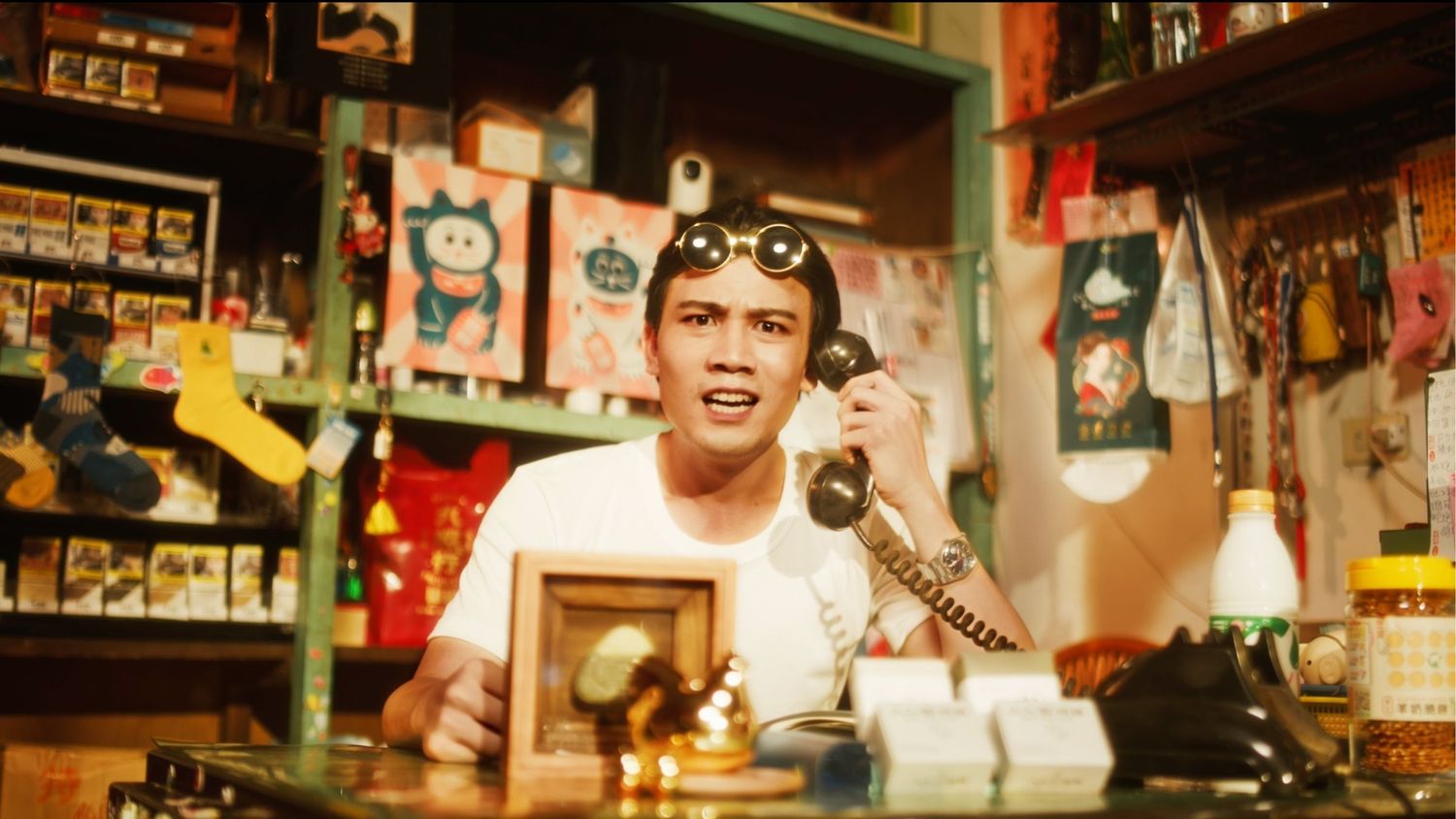 A person works behind the counter at a convenience store, surrounded by vintage decor and a corded telephone.