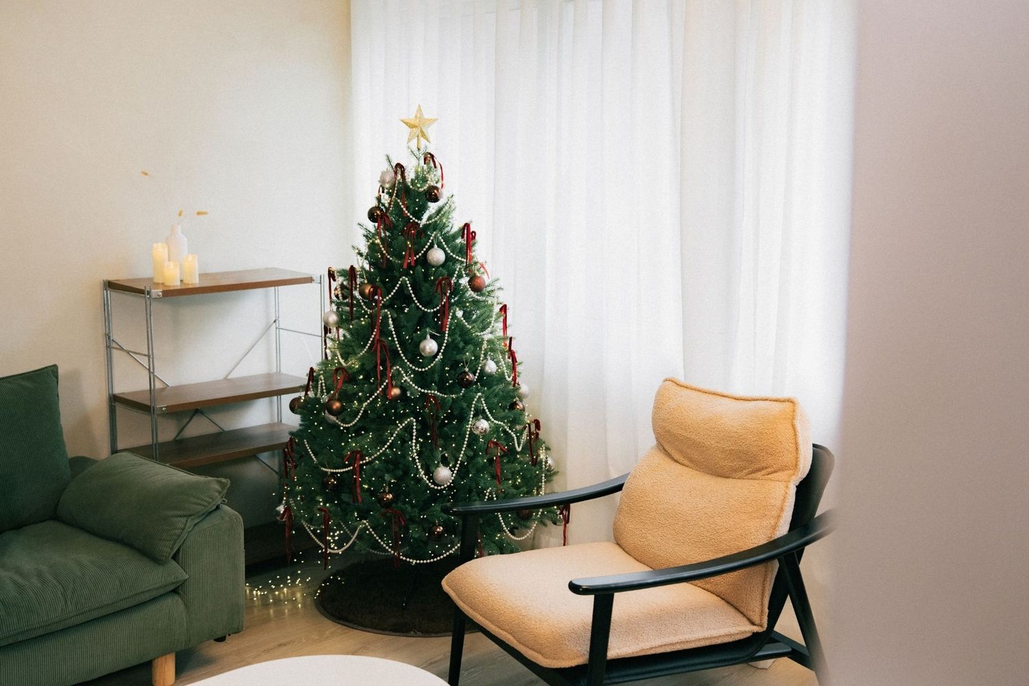 Decorated Christmas tree with ornaments and star topper in a cozy living room with green sofa and armchair.