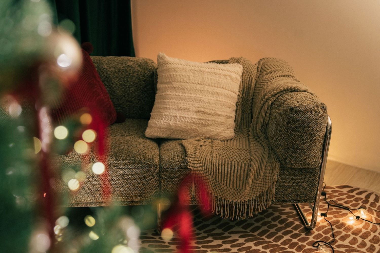 Cozy armchair with knit pillow and blanket beside a decorated Christmas tree with warm fairy lights.