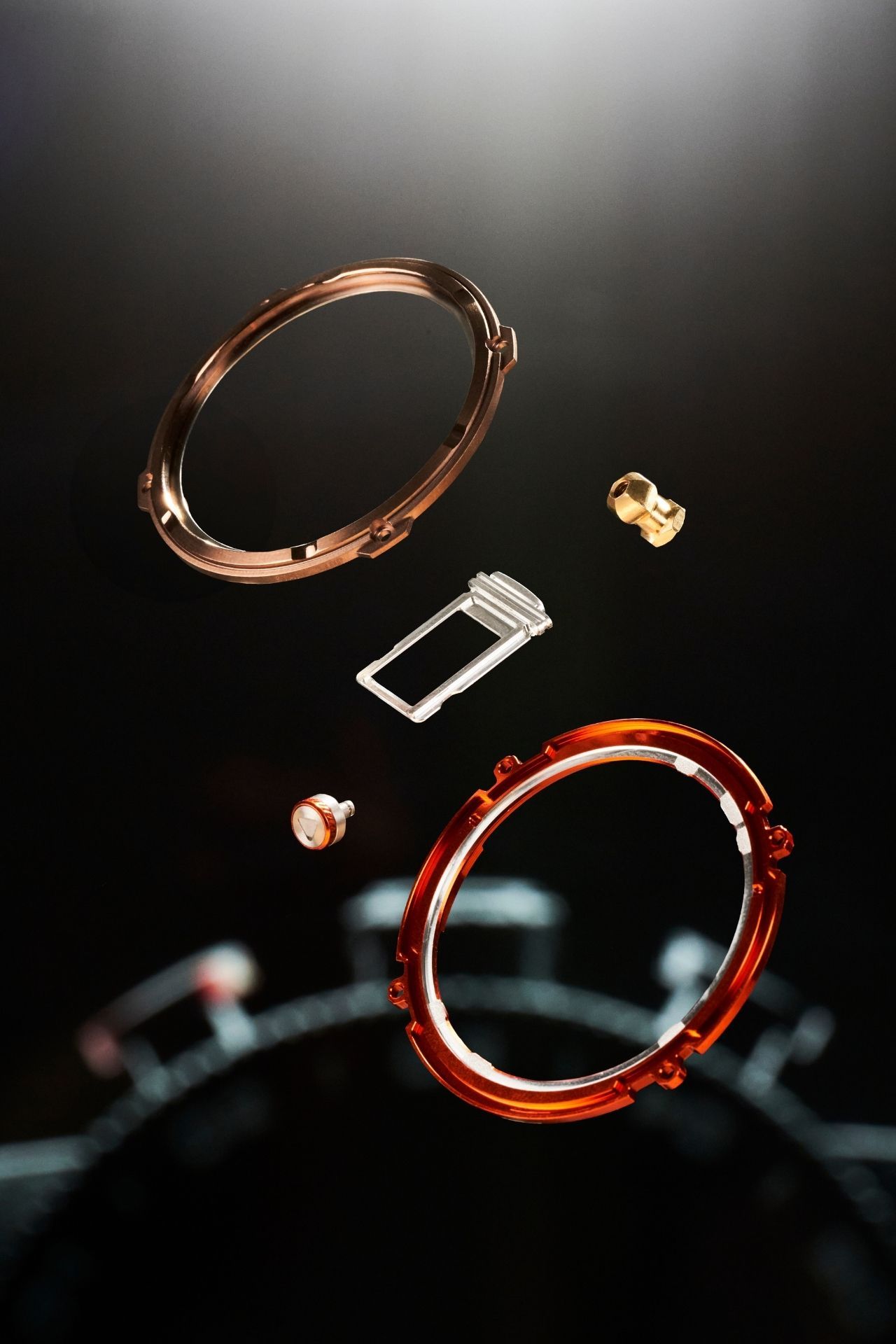 Artistic close-up sequence showing the disassembly of red and copper-colored metallic components against a dark background.