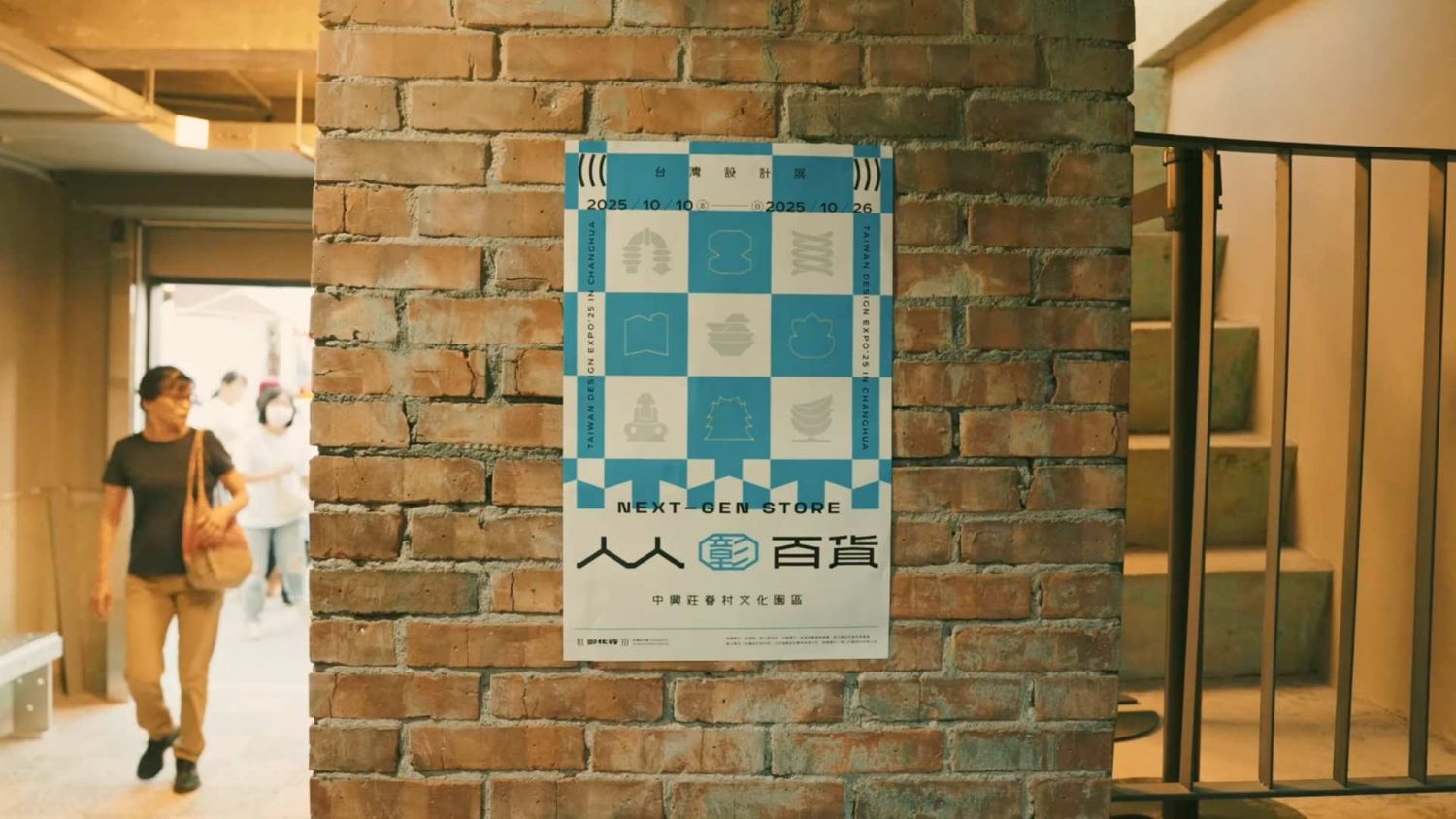 A blue and white checkered poster hangs on an exposed brick wall near a doorway in an indoor space.