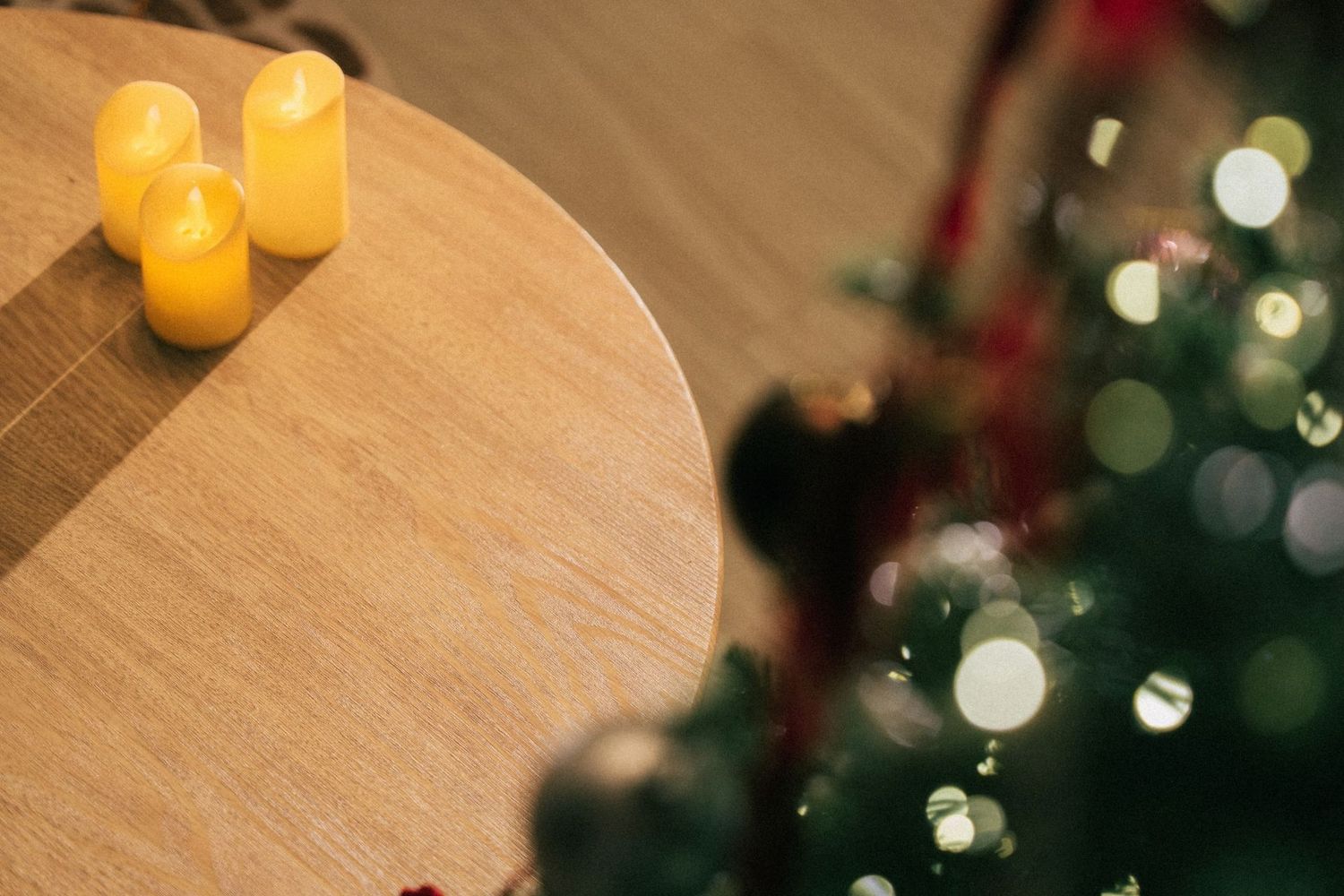 Three glowing LED candles on a wooden table beside a decorated Christmas tree with bokeh lights.