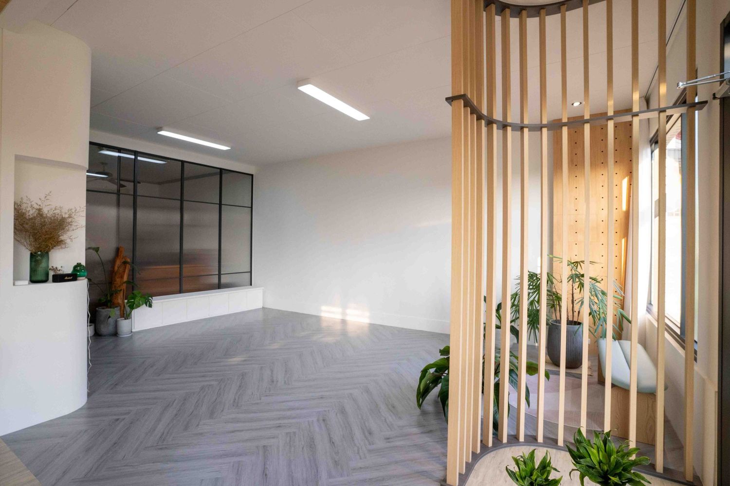 Modern dining area with wooden slat room divider, herringbone flooring, and white walls in a minimalist space.