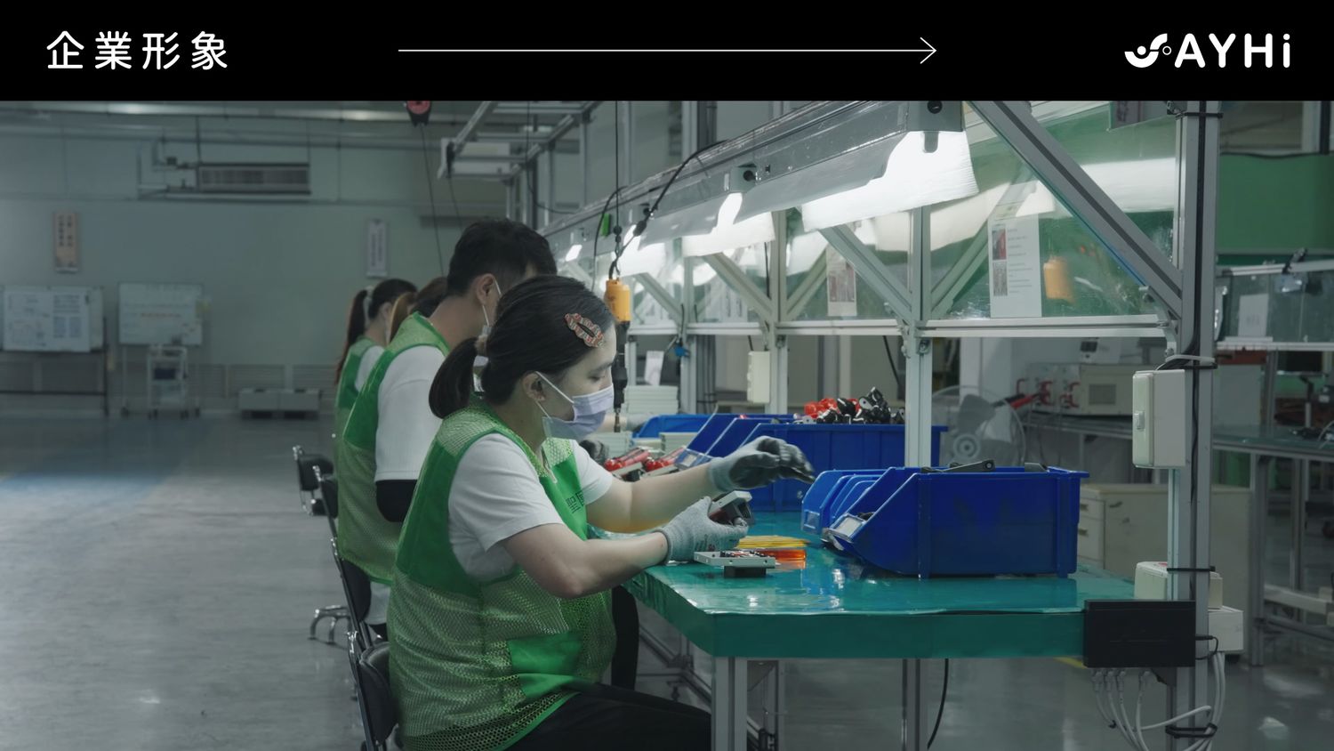 Workers in green uniforms assembling electronics at a factory production line in a modern manufacturing facility.