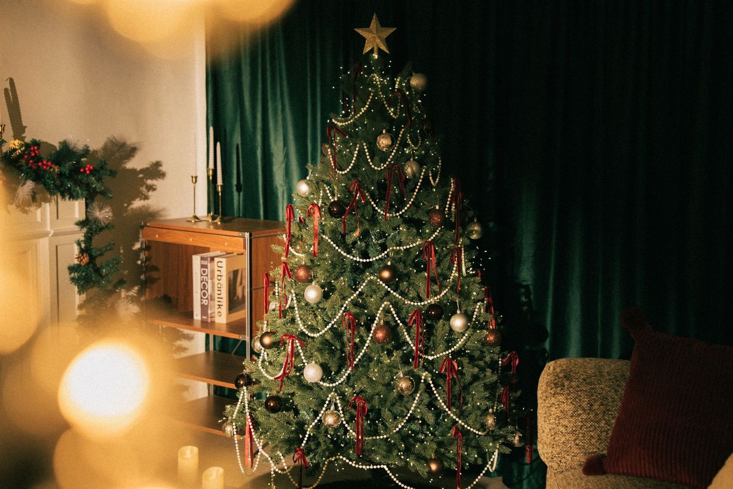 Decorated Christmas tree with gold star topper, red ribbons, and ornaments in a cozy living room with green curtains.