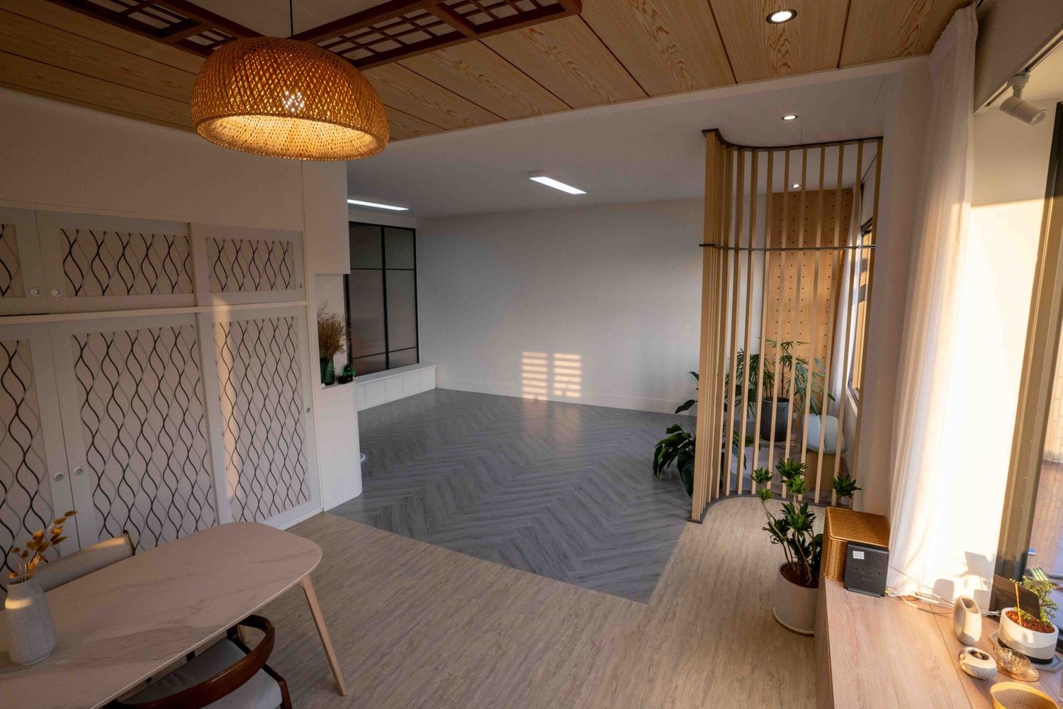 A modern open floor plan living room features white walls, hanging pendant lights, and contemporary decor with natural lighting.