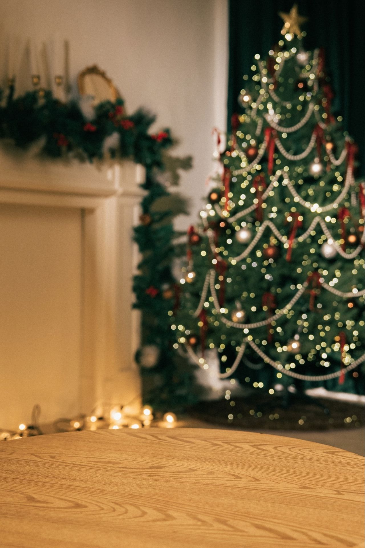 Festive Christmas tree with bokeh lights beside a decorated fireplace mantel on a warm wooden floor.
