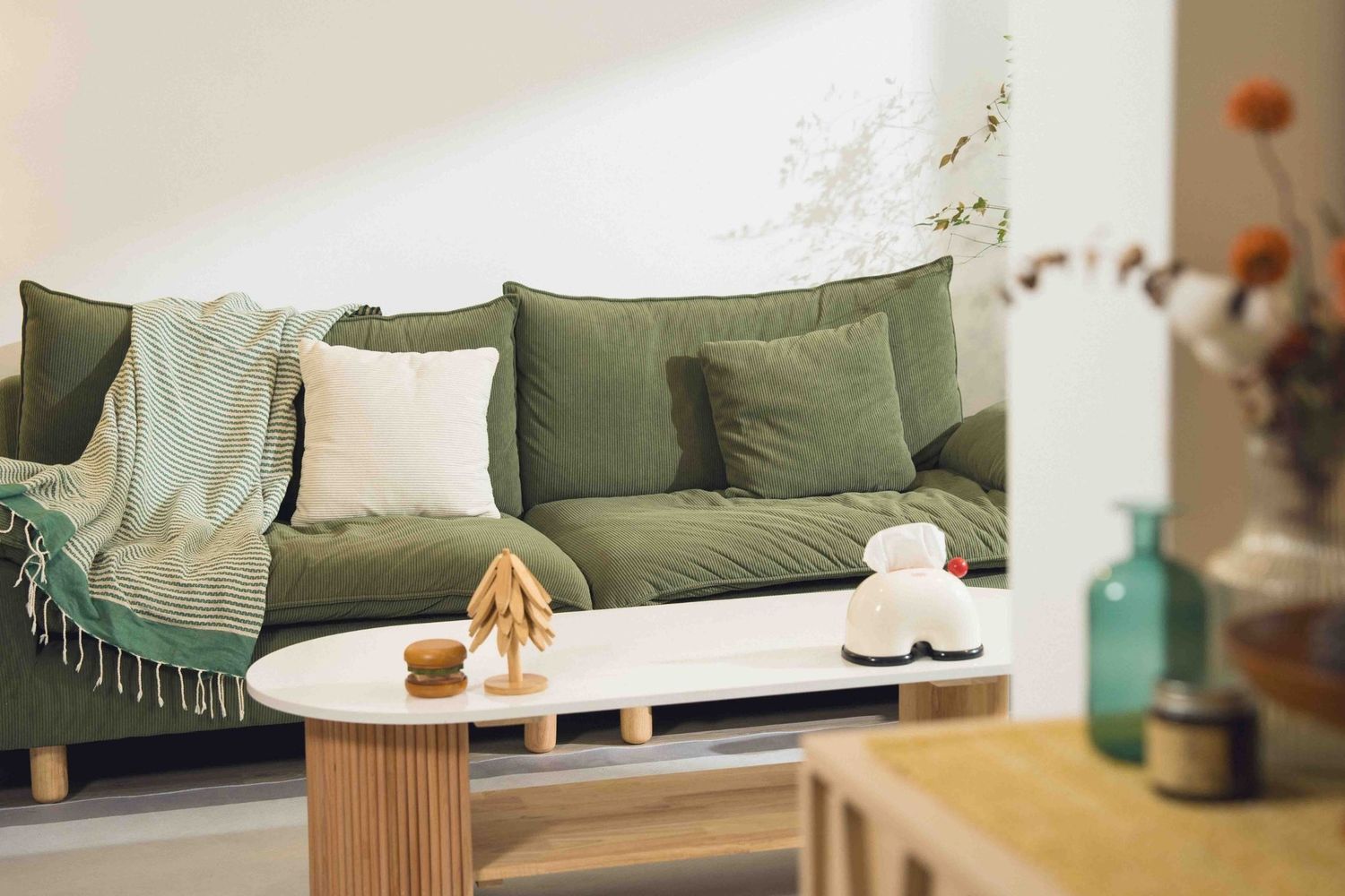 Modern living room decorated in sage green and white with a cozy sofa and round wooden coffee table.