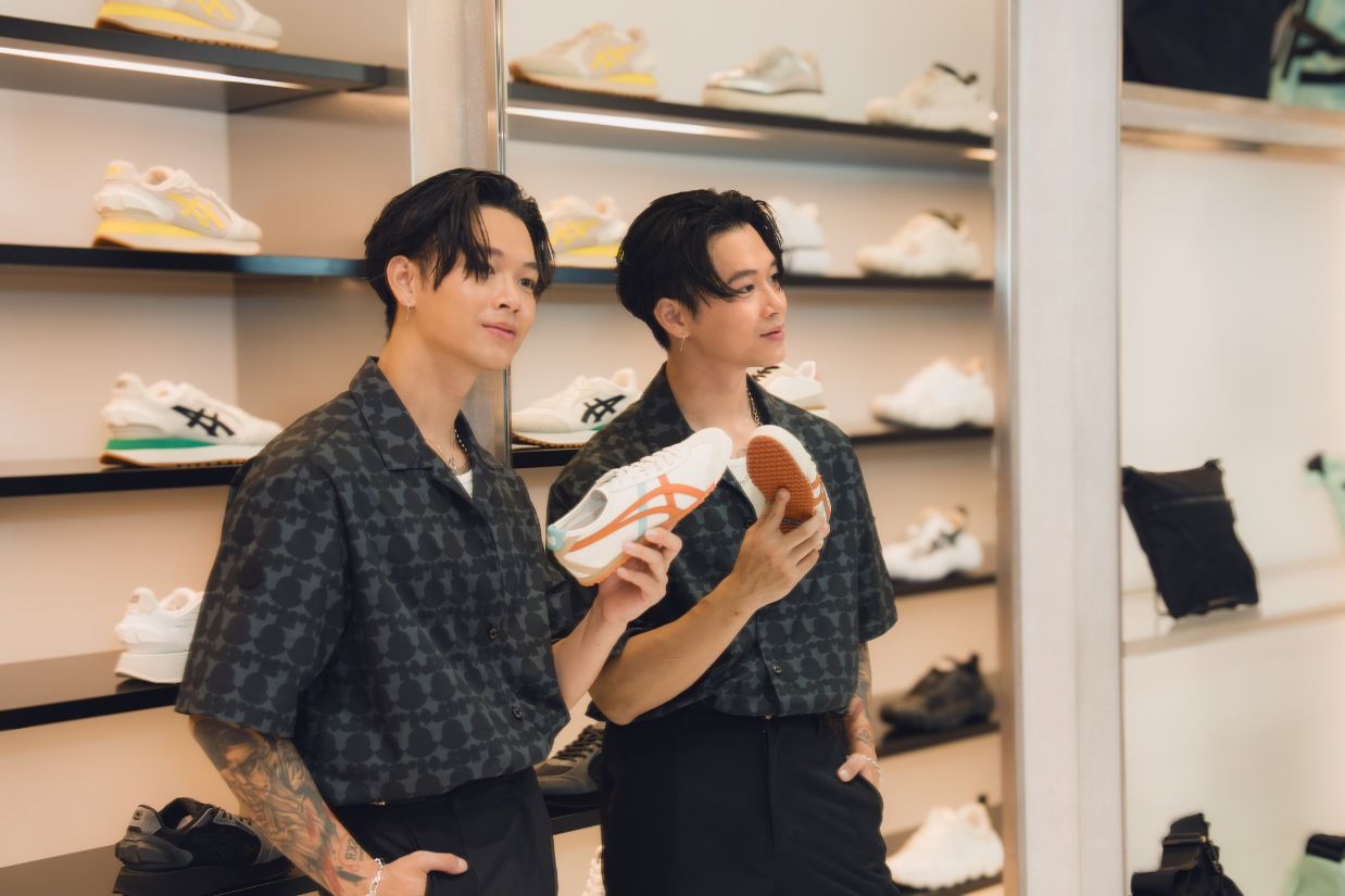 Two people wearing matching dark patterned shirts browse shoes at a retail store with shelves of sneakers.