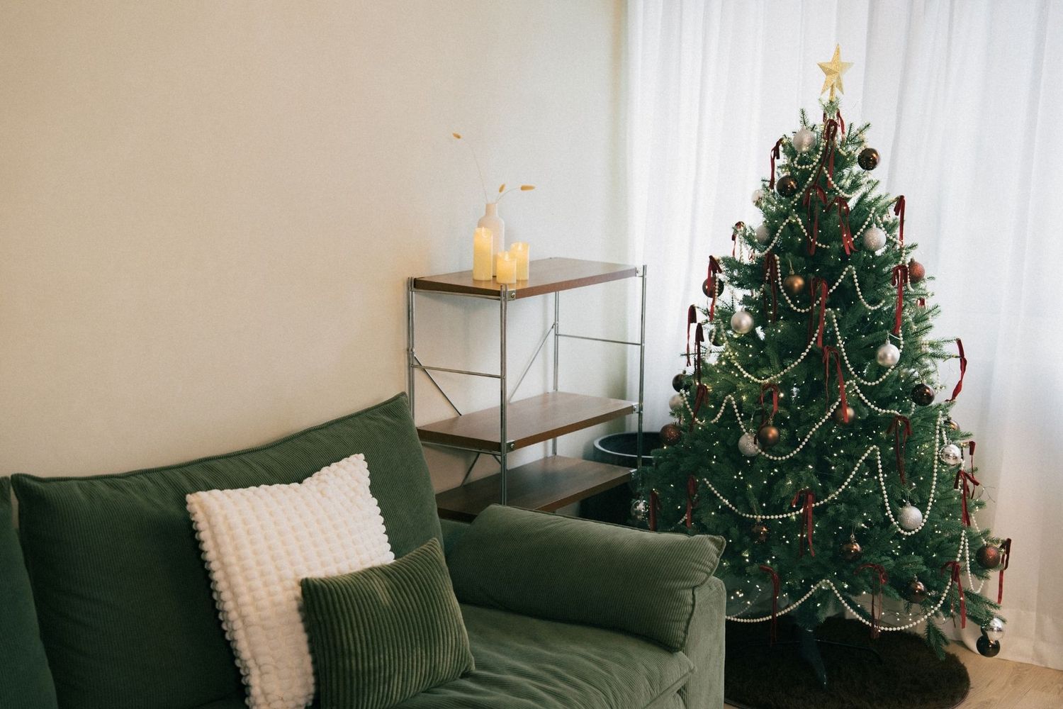 Cozy living room with green velvet armchair, decorated Christmas tree with ornaments, and a wooden shelf unit.