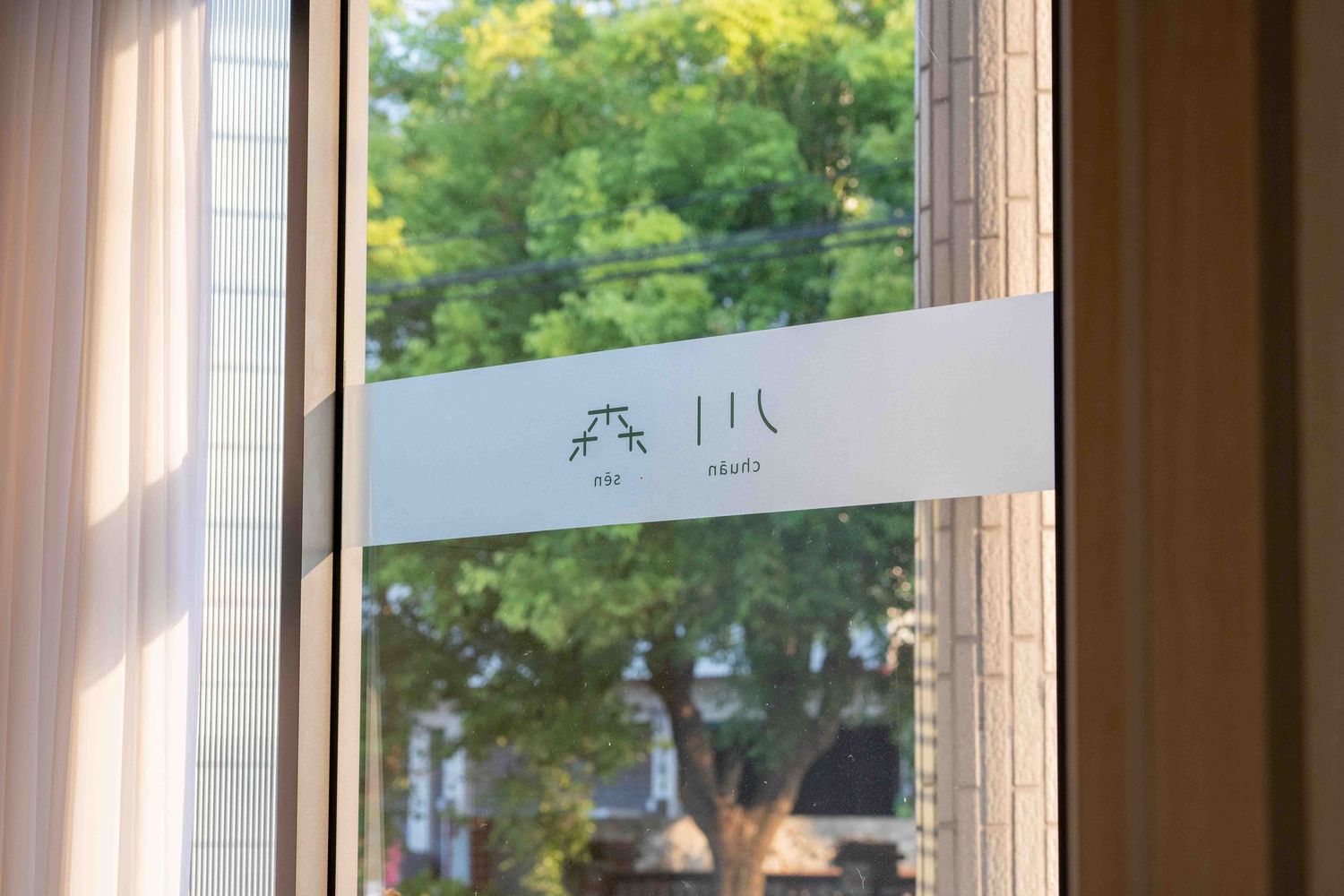 Frosted glass window decal with minimalist design seen against green trees in daylight background.