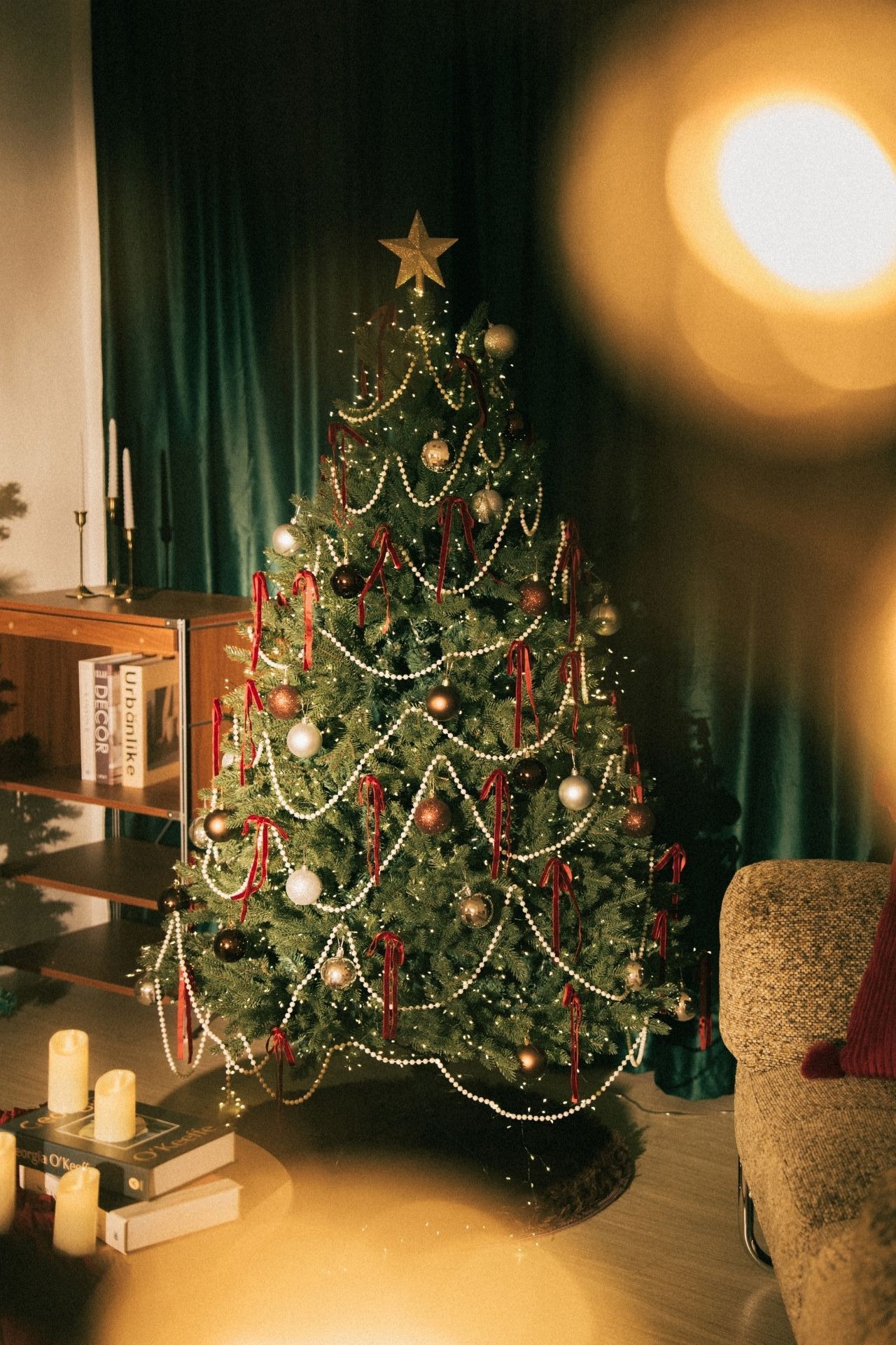 Beautifully decorated Christmas tree with gold star, pearl garlands, red ribbons, and ornaments in a cozy warmly lit living room.