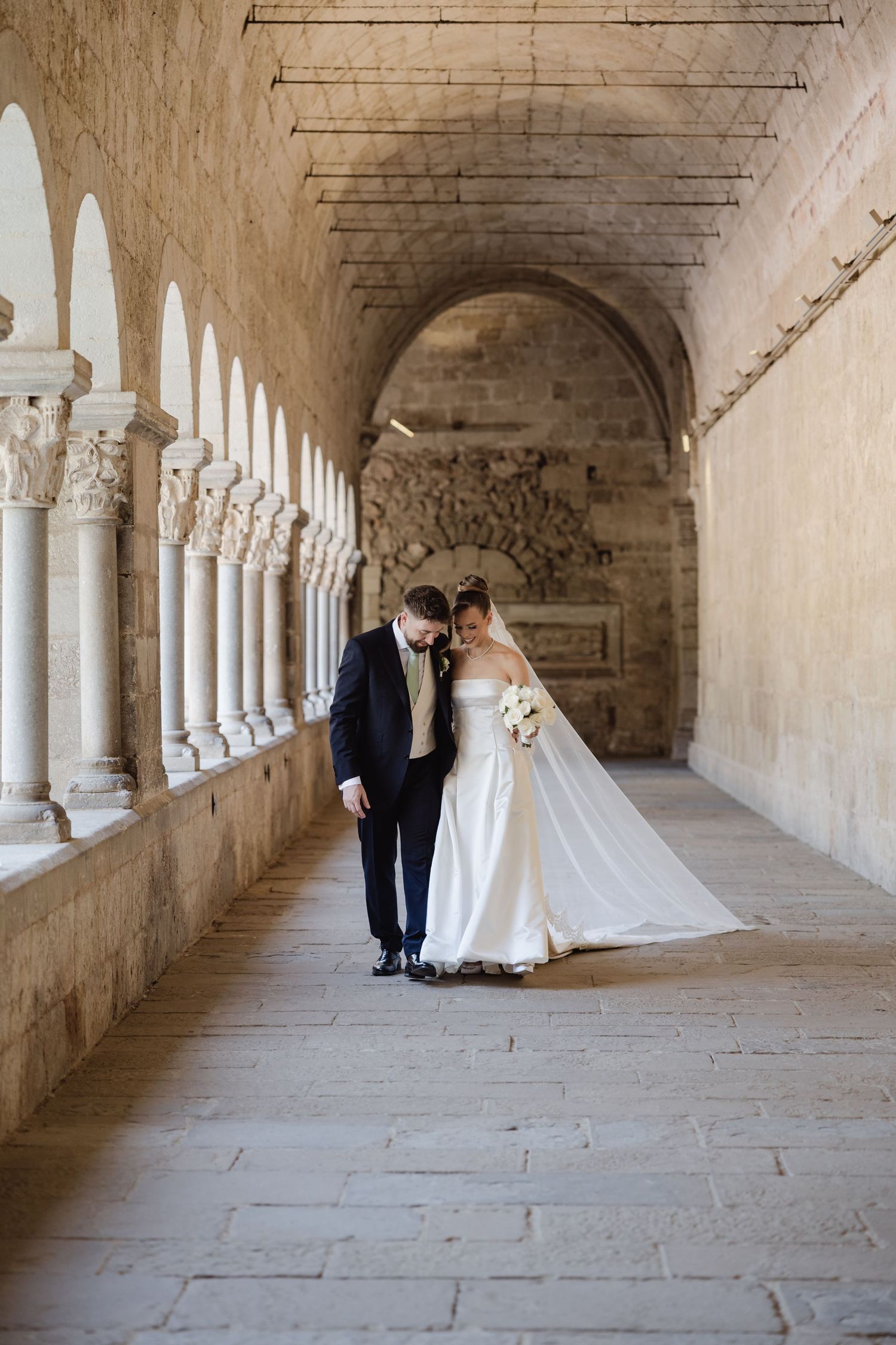 Bride and groom share a romantic moment in a historic stone archway corridor on their wedding day.