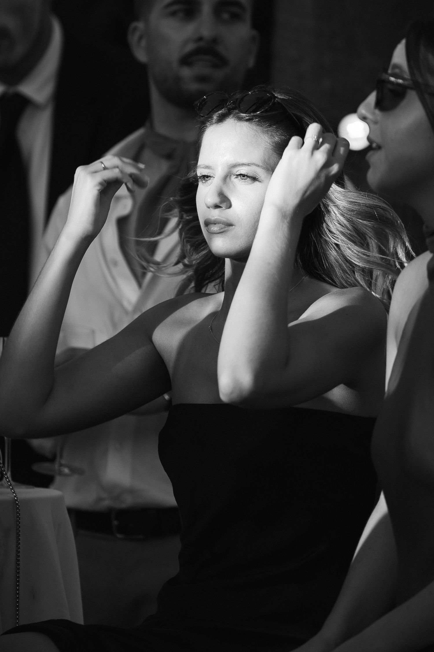 Elegant woman in black dress adjusting hair at formal event in black and white photography.