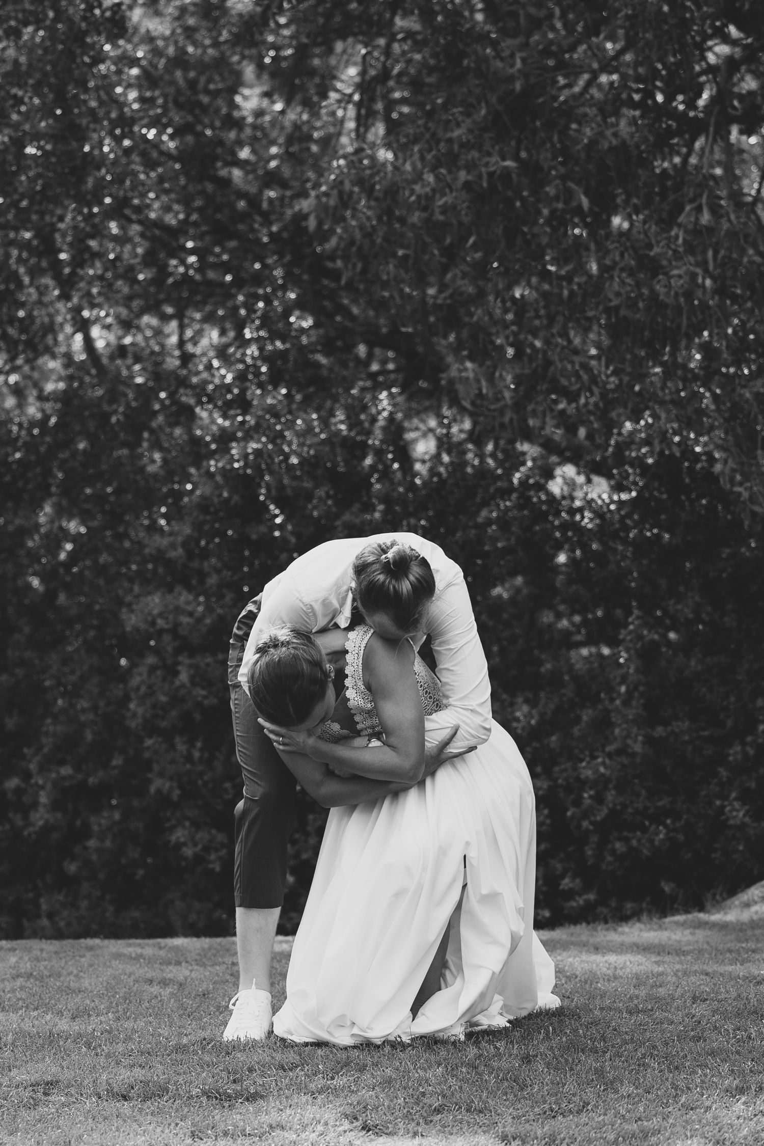 Black and white photo of bride and groom sharing a romantic embrace on a green lawn with trees.