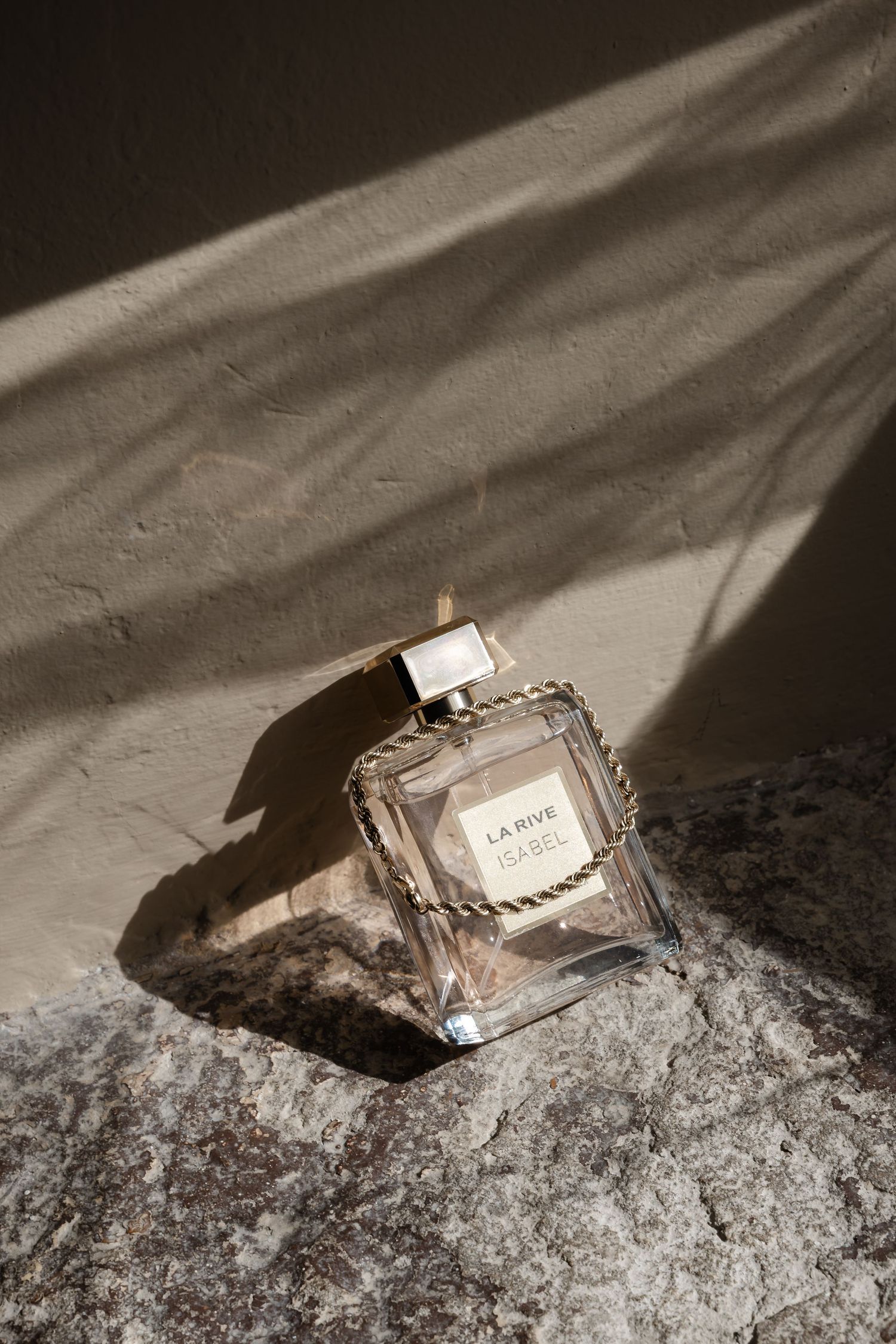 La Rive Isabel perfume bottle with gold chain detail on a stone surface with warm sunlight and shadows.