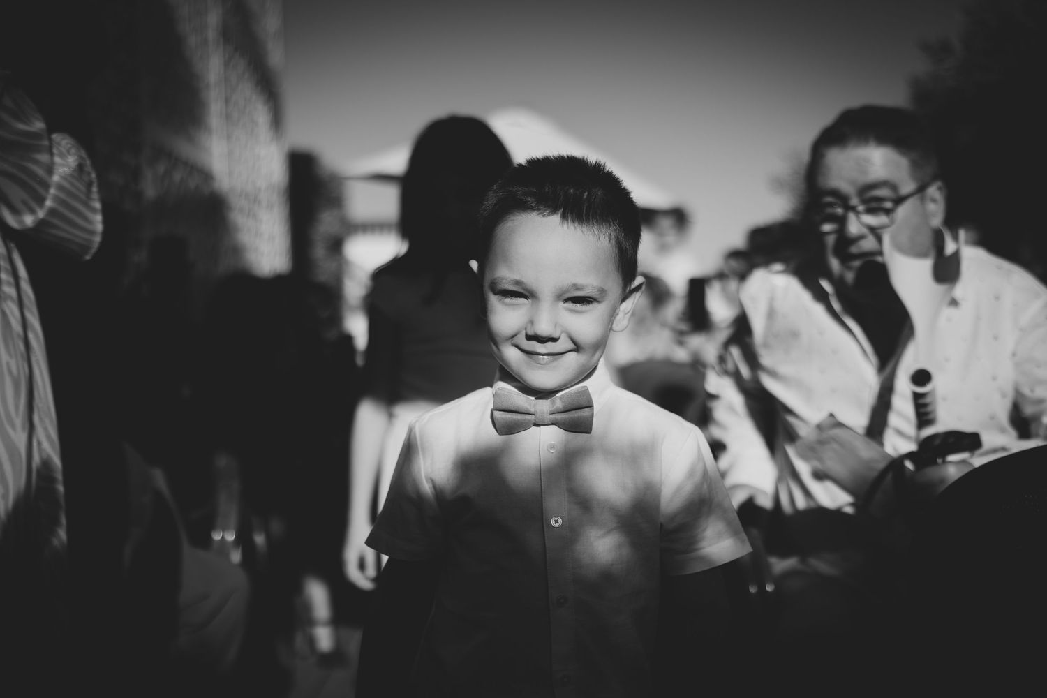 Smiling young boy in white shirt and bow tie at a wedding celebration, black and white photo.