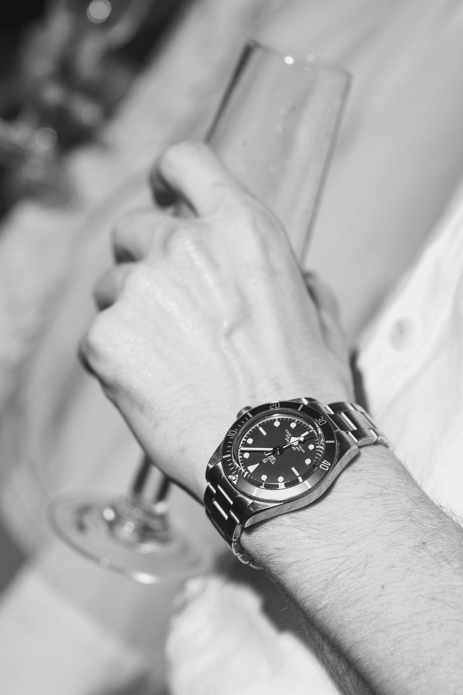 Black and white close-up of a man's wrist wearing a luxury dive watch while holding a champagne flute.
