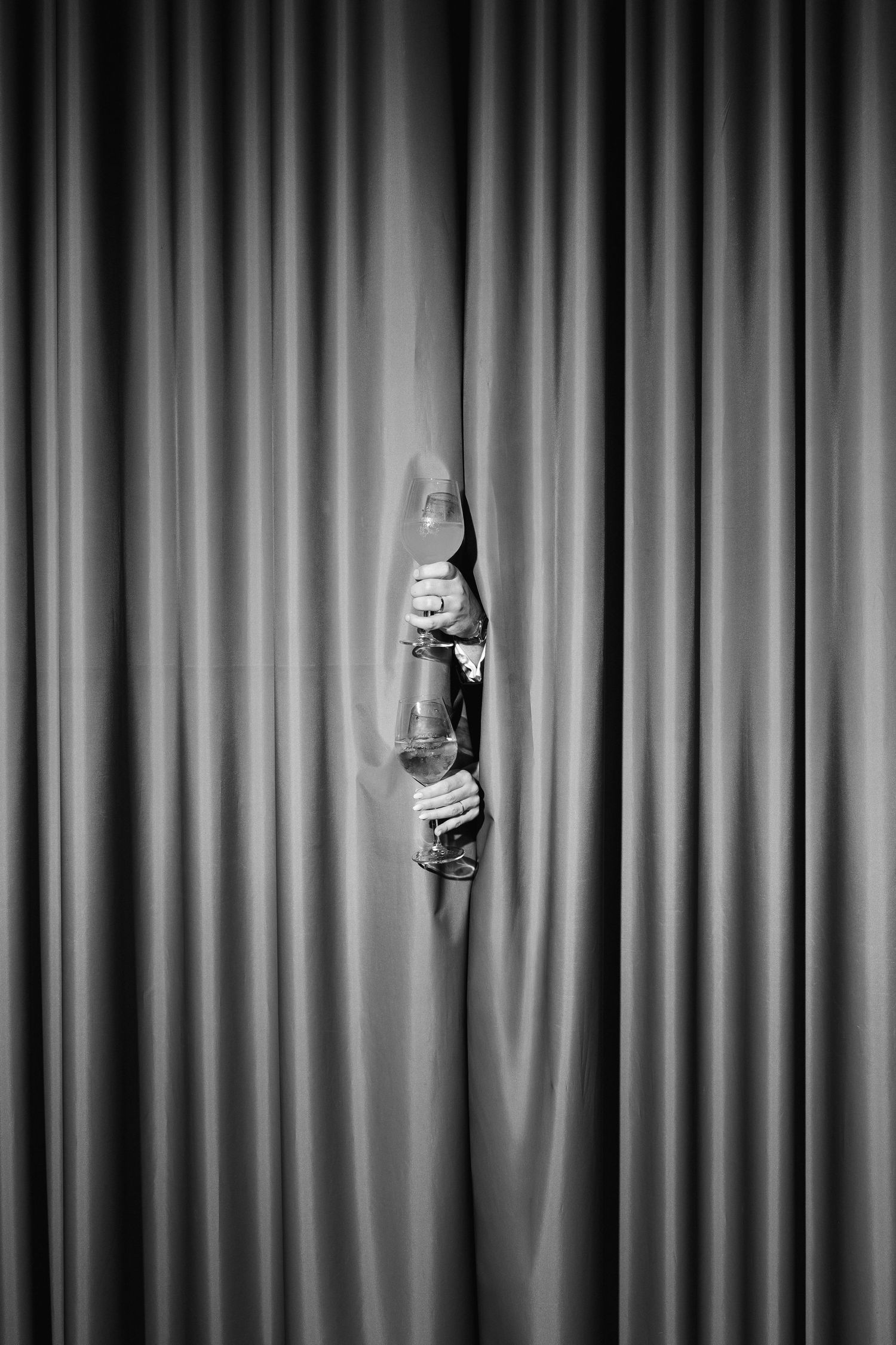 A hand emerges through velvet stage curtains holding a vintage oil lantern in a dramatic black and white photo.