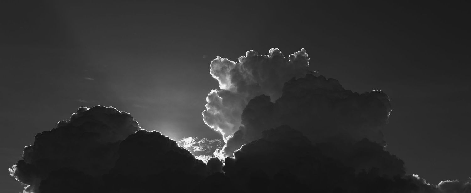 Dramatic black and white panoramic photo of billowing storm clouds against a dark sky.