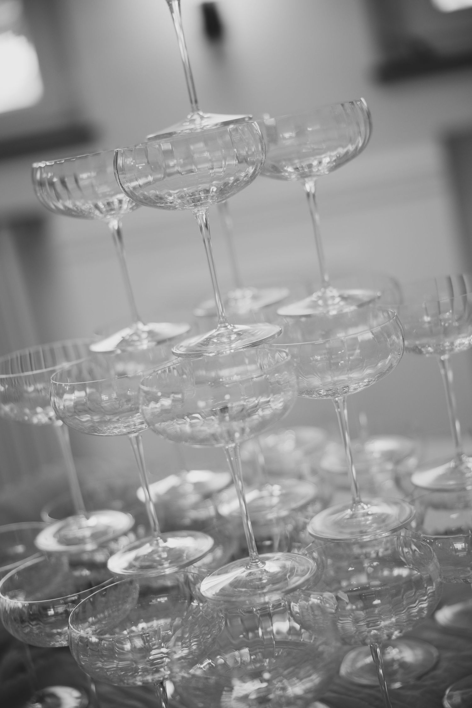 Black and white photo of an elegant pyramid tower of champagne coupe glasses at a wedding.