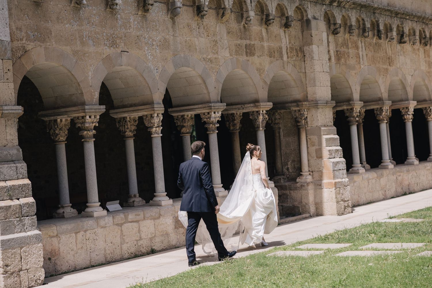 Bride and groom walking through a historic stone archway colonnade on their wedding day.