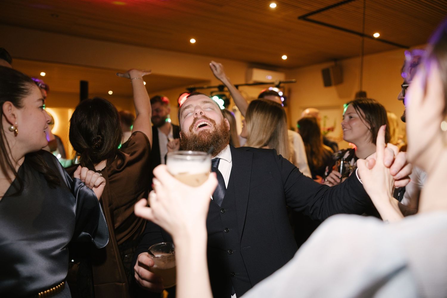 Guests celebrating at a lively wedding reception, dancing and holding drinks on the dance floor.