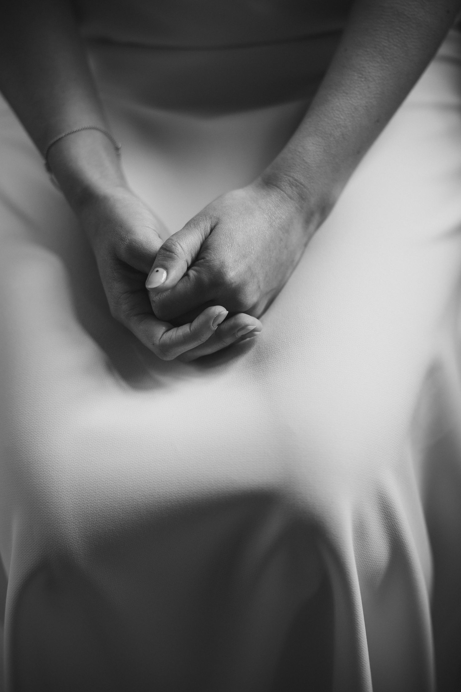 Close-up black and white photo of a bride's hands clasped together over her white wedding dress.
