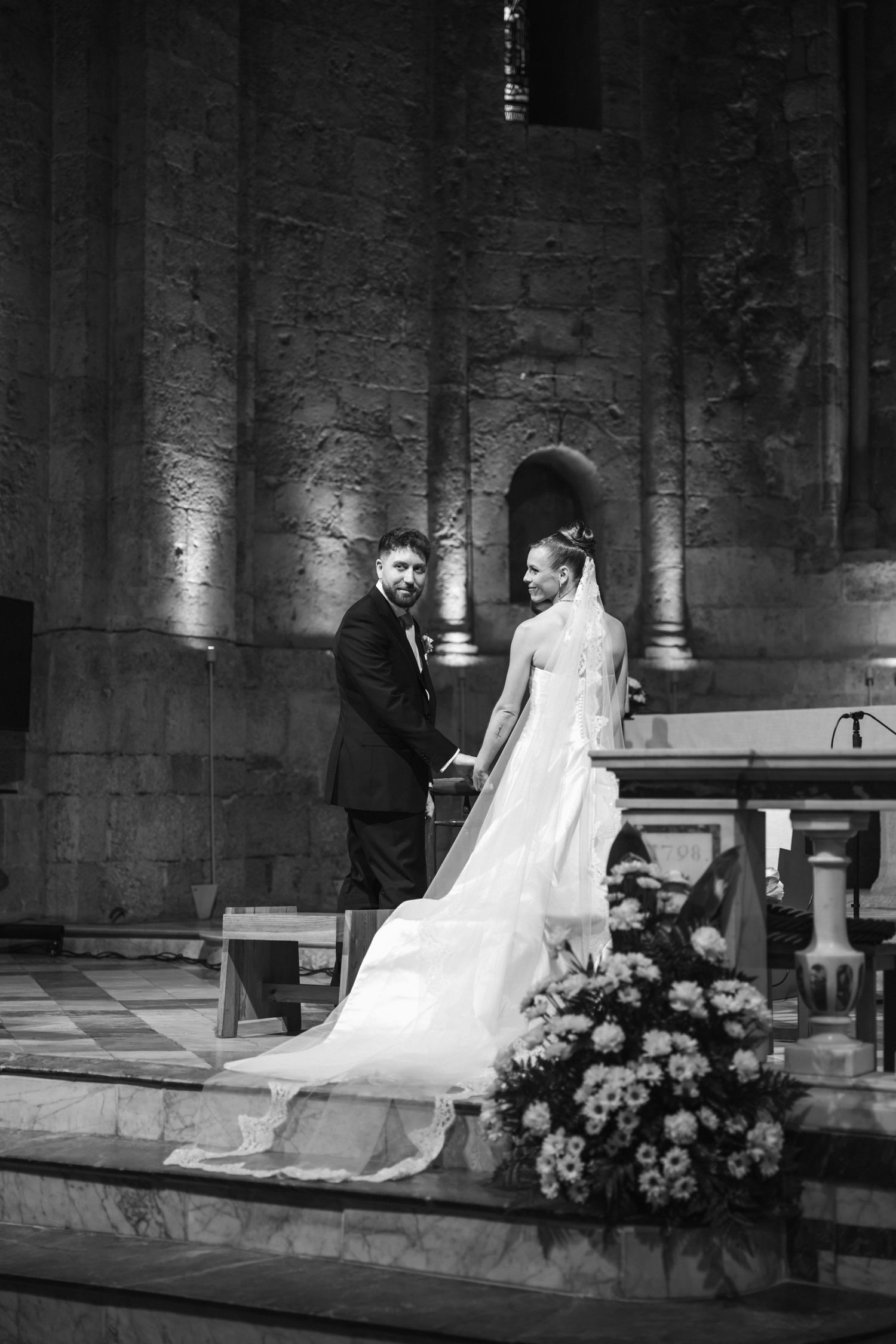 Black and white photo of a bride and groom holding hands at the altar during a church wedding ceremony.