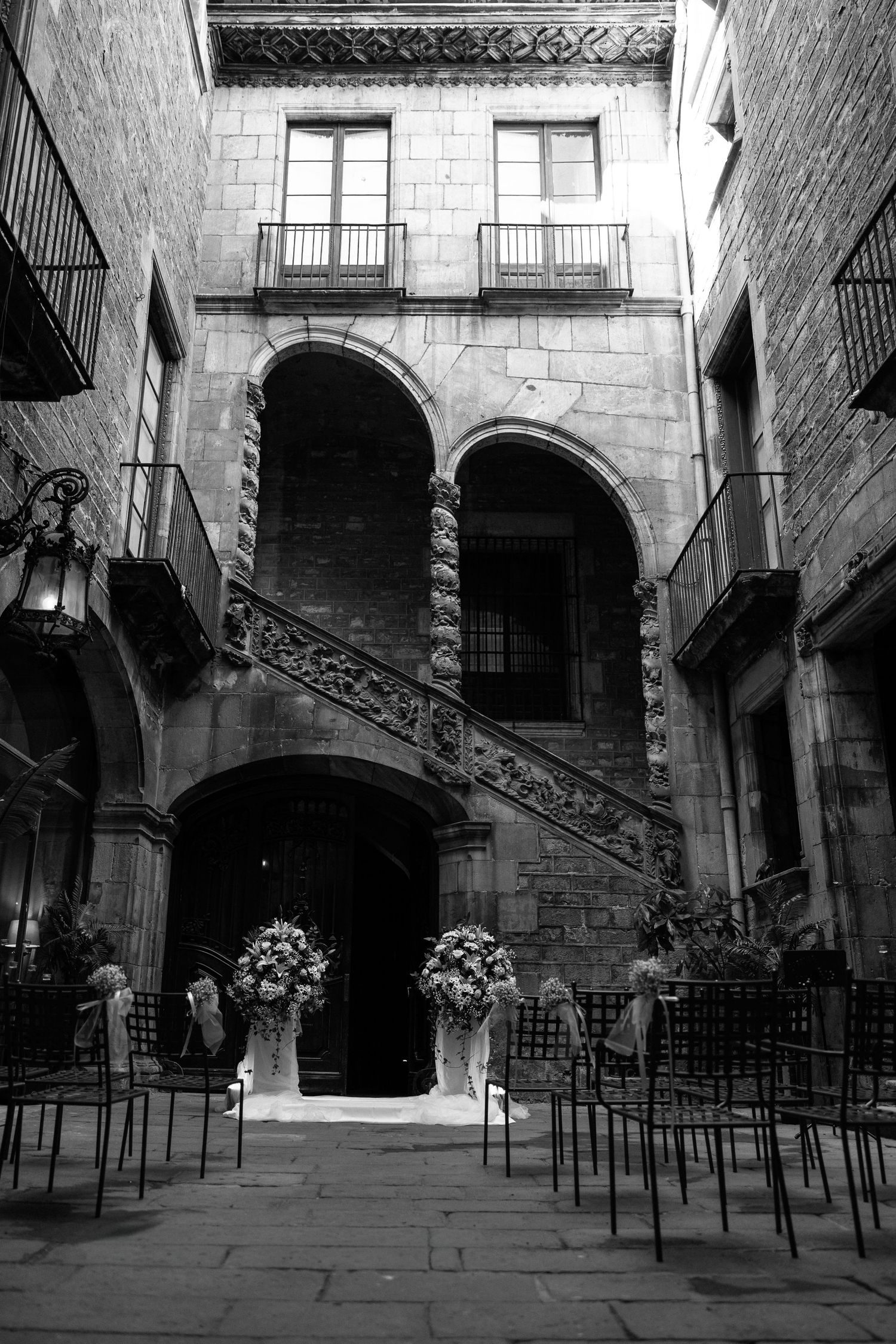 Black and white courtyard wedding venue with ornate arches, floral arrangements, and rows of chairs.