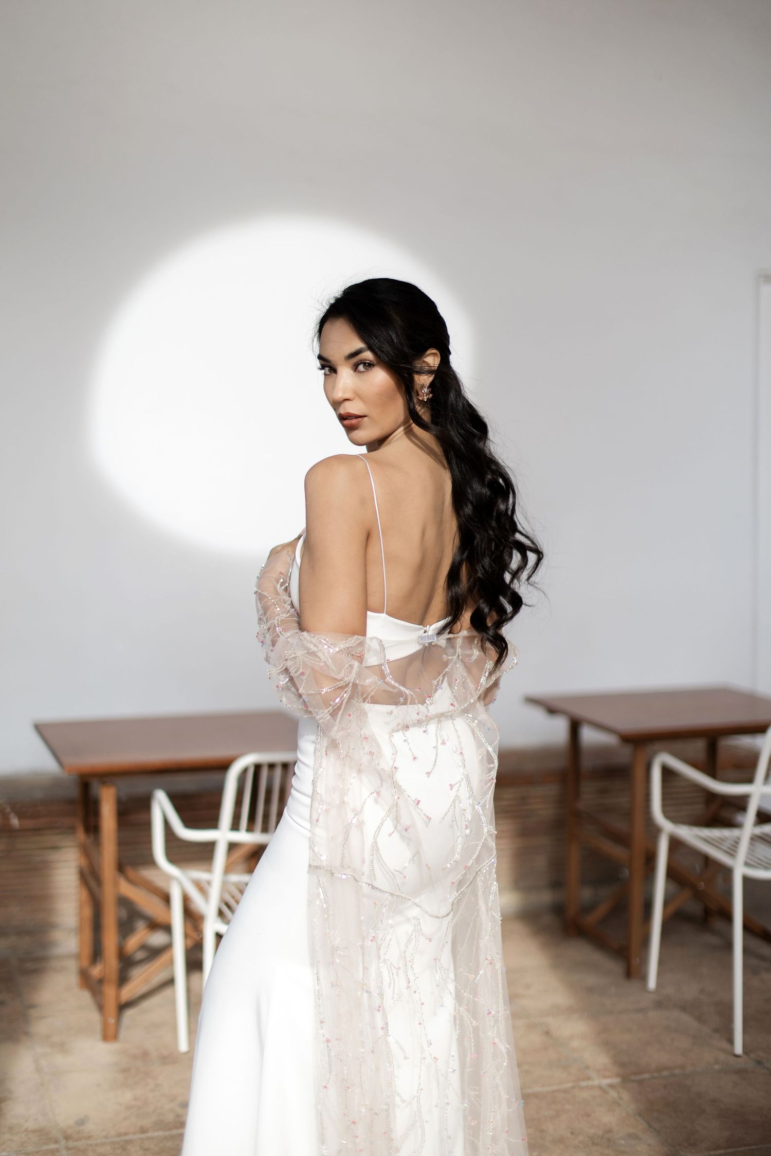 Bride in backless lace wedding gown with flowing train looking over shoulder indoors.