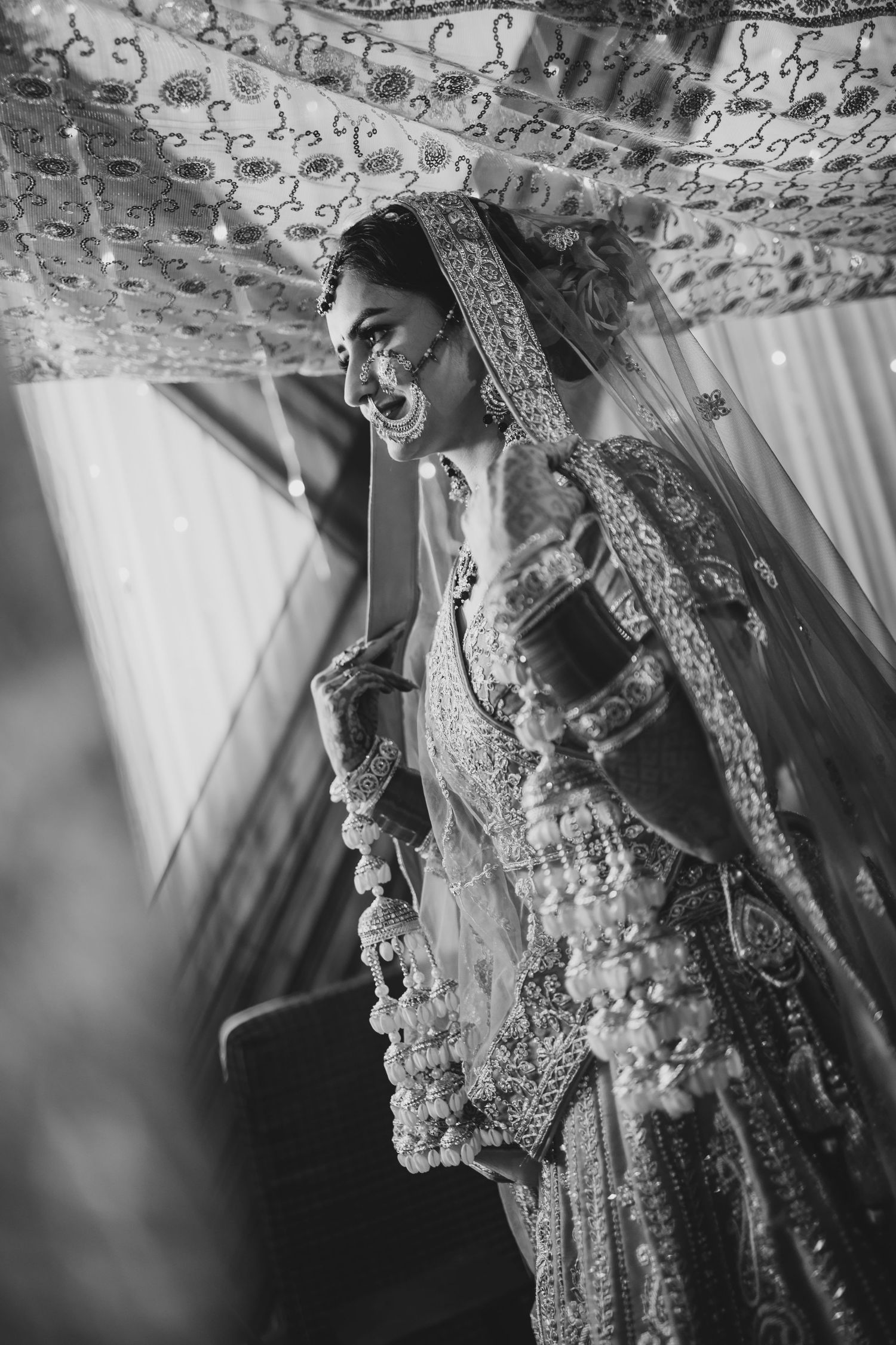 Indian bride in ornate traditional bridal lehenga and jewelry in black and white portrait.