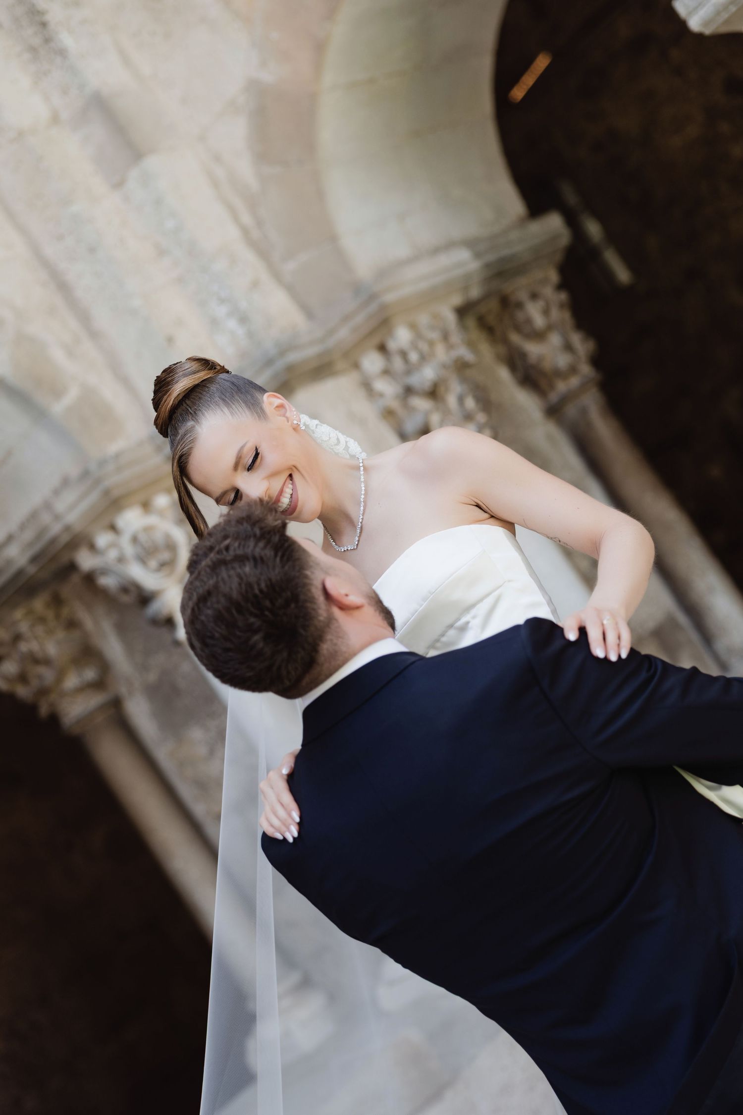 Bride and groom share a romantic moment, with the smiling bride in a white gown and veil held by her suited groom.