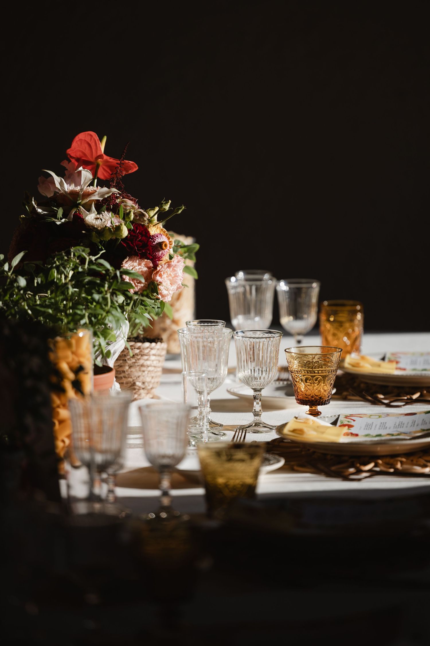 Elegant wedding table setting with crystal glassware, amber goblets, and red floral centerpiece.