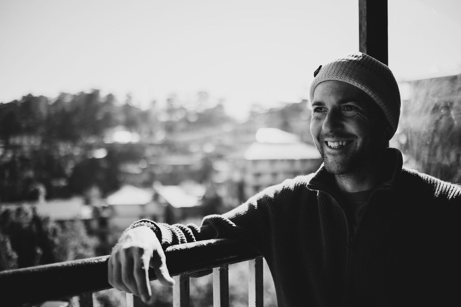 Happy man in beanie leaning on balcony railing.