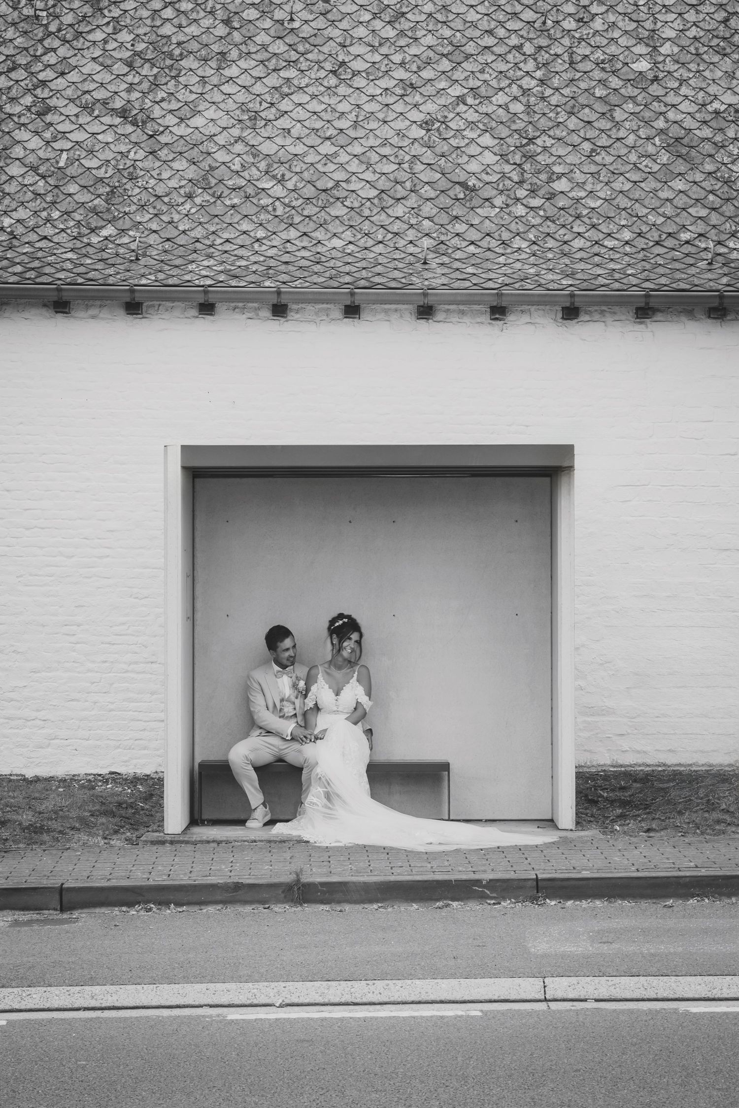 Black and white portrait of wedding couple sitting together in a minimalist architectural alcove outdoors.