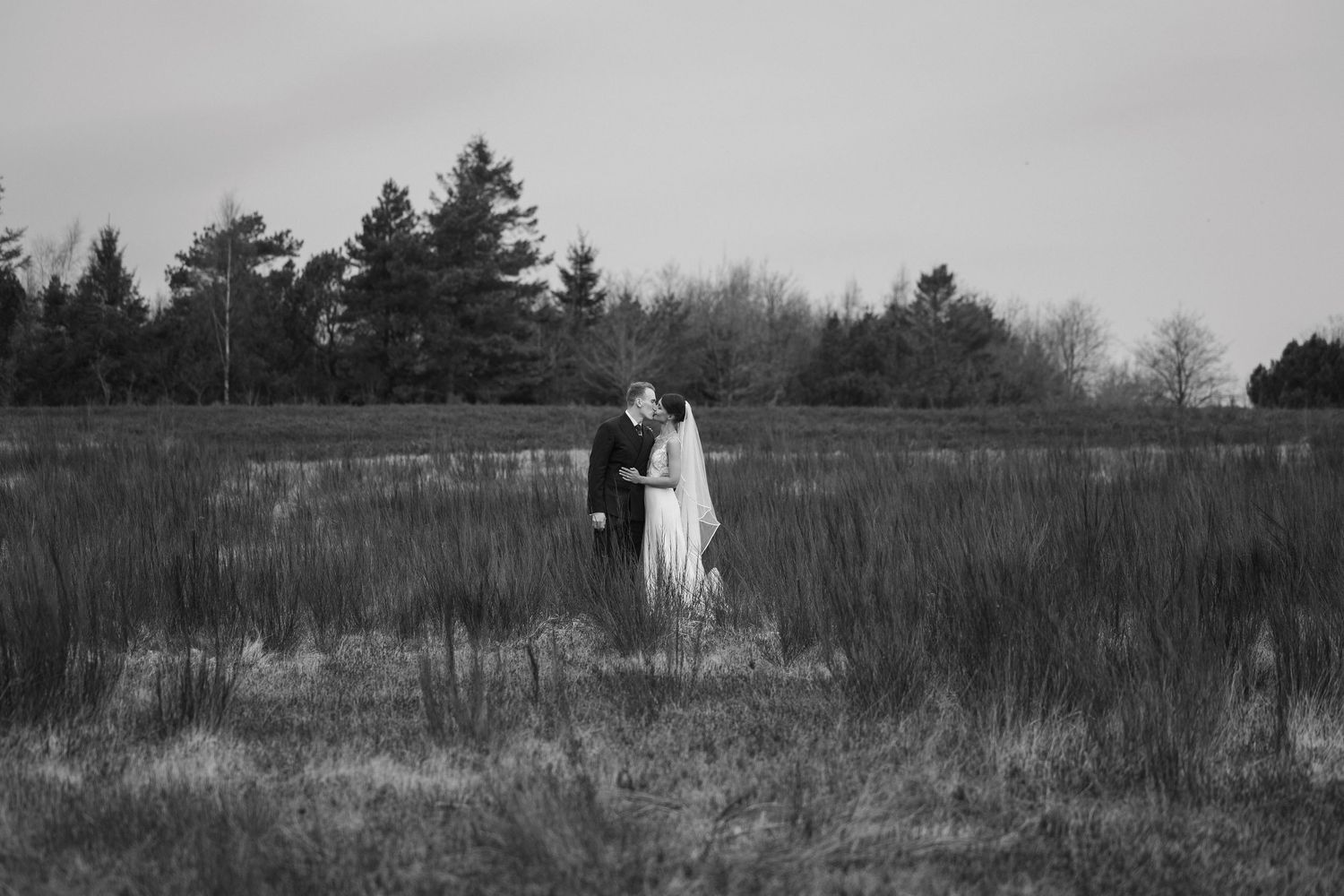 Black and white photo of a bride and groom sharing a romantic moment in an open field.