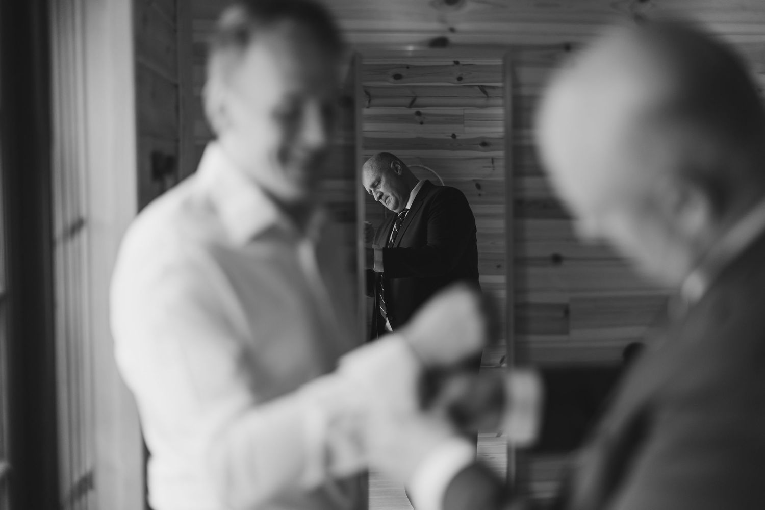 Black and white photo of groomsmen preparing for a wedding ceremony in a rustic wooden room.