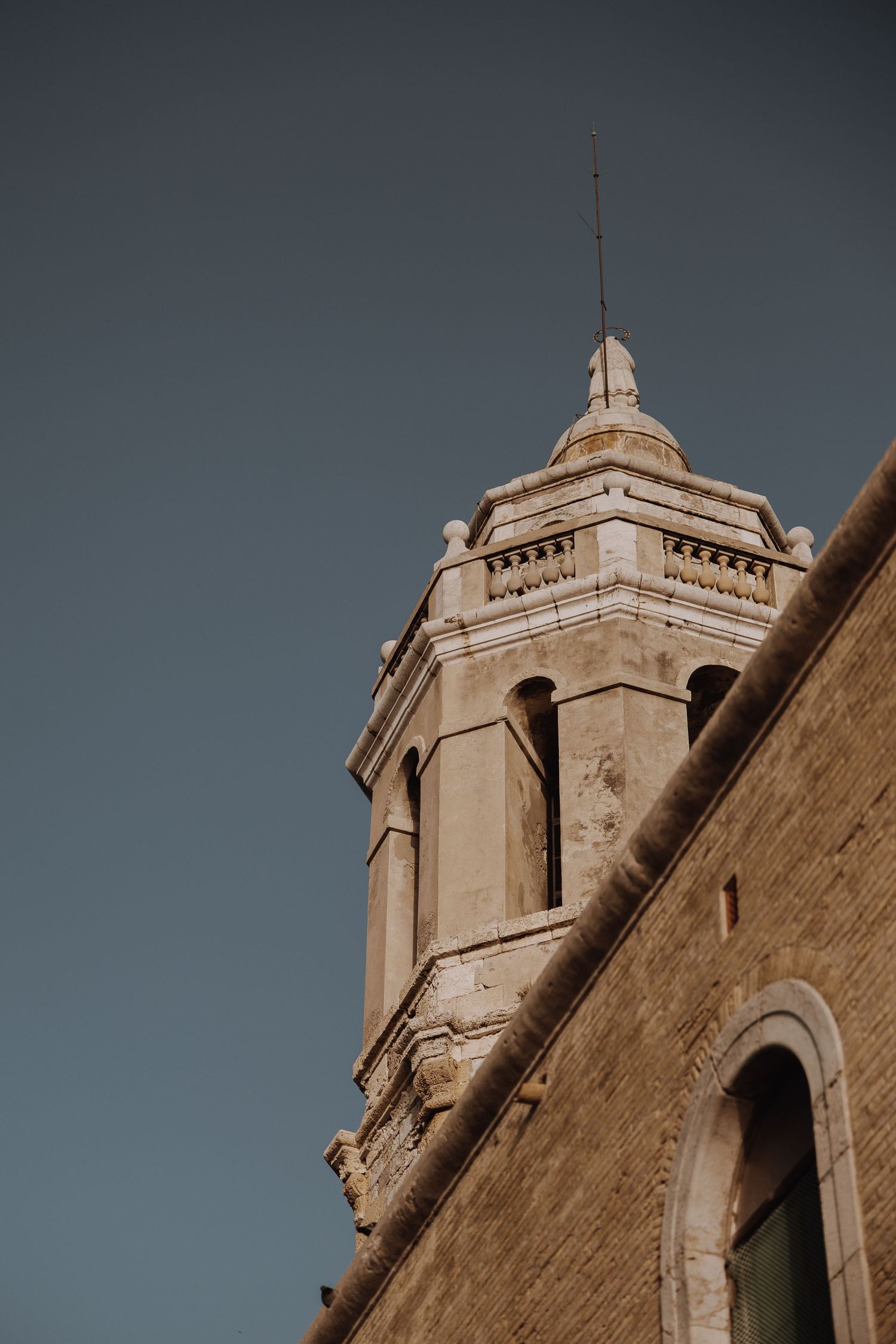 Historic stone church bell tower with arched windows against a clear blue sky.