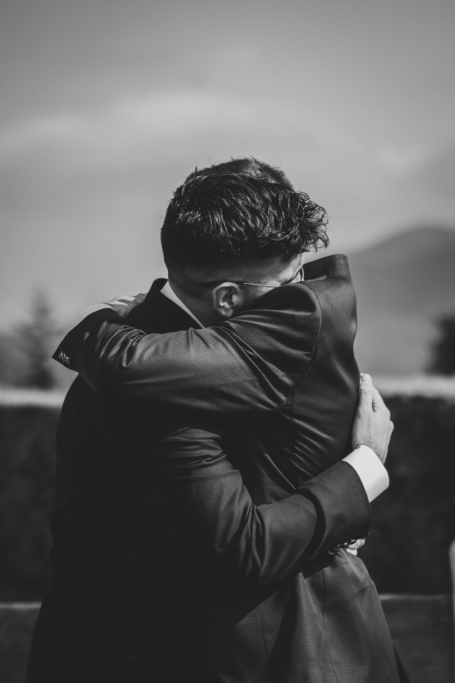 Black and white photo of two grooms sharing an emotional embrace outdoors.