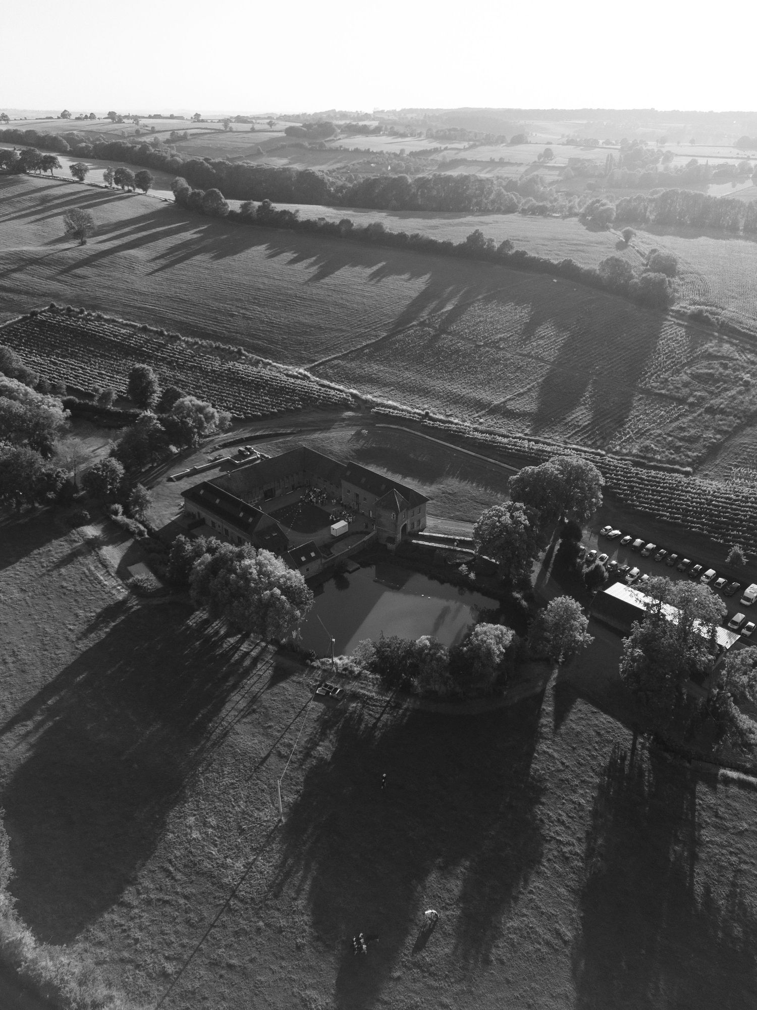 Aerial black and white photo of a rural farmstead surrounded by trees and patchwork fields in the countryside.
