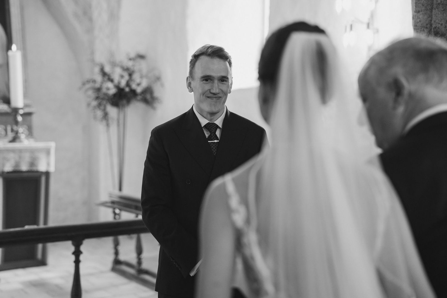 Emotional groom smiling at bride walking down the aisle in a classic church ceremony.