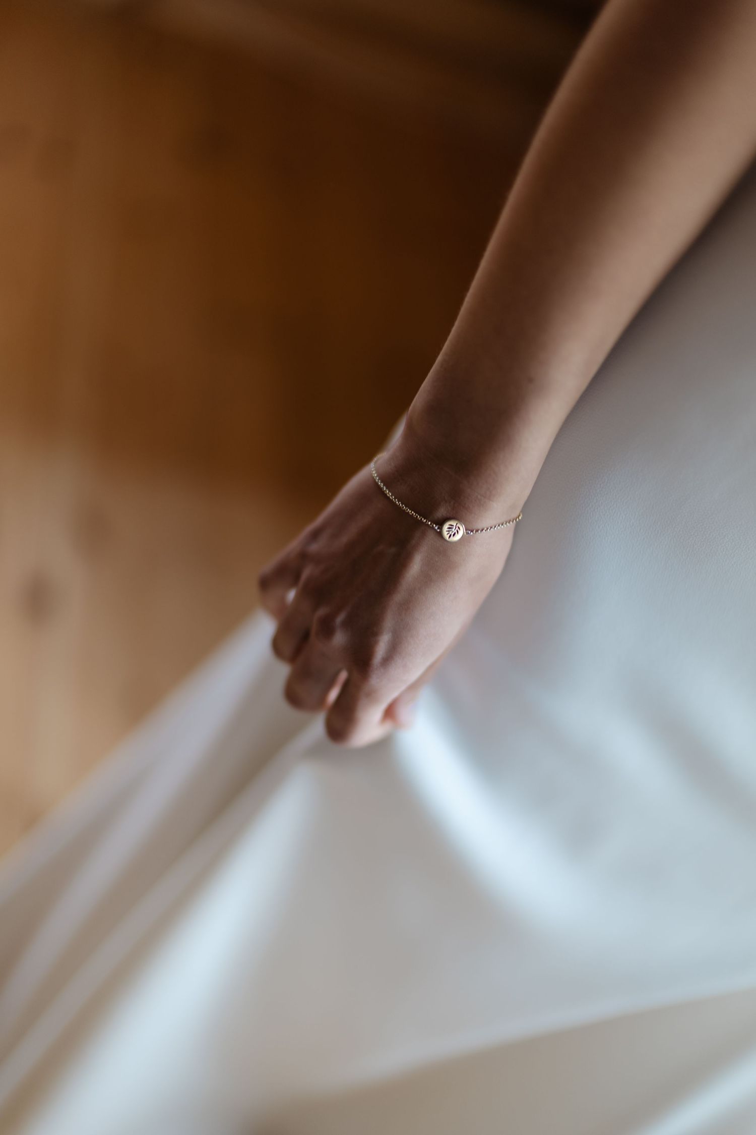 Close-up of a bride's hand wearing a delicate silver bracelet, resting on white wedding dress fabric.