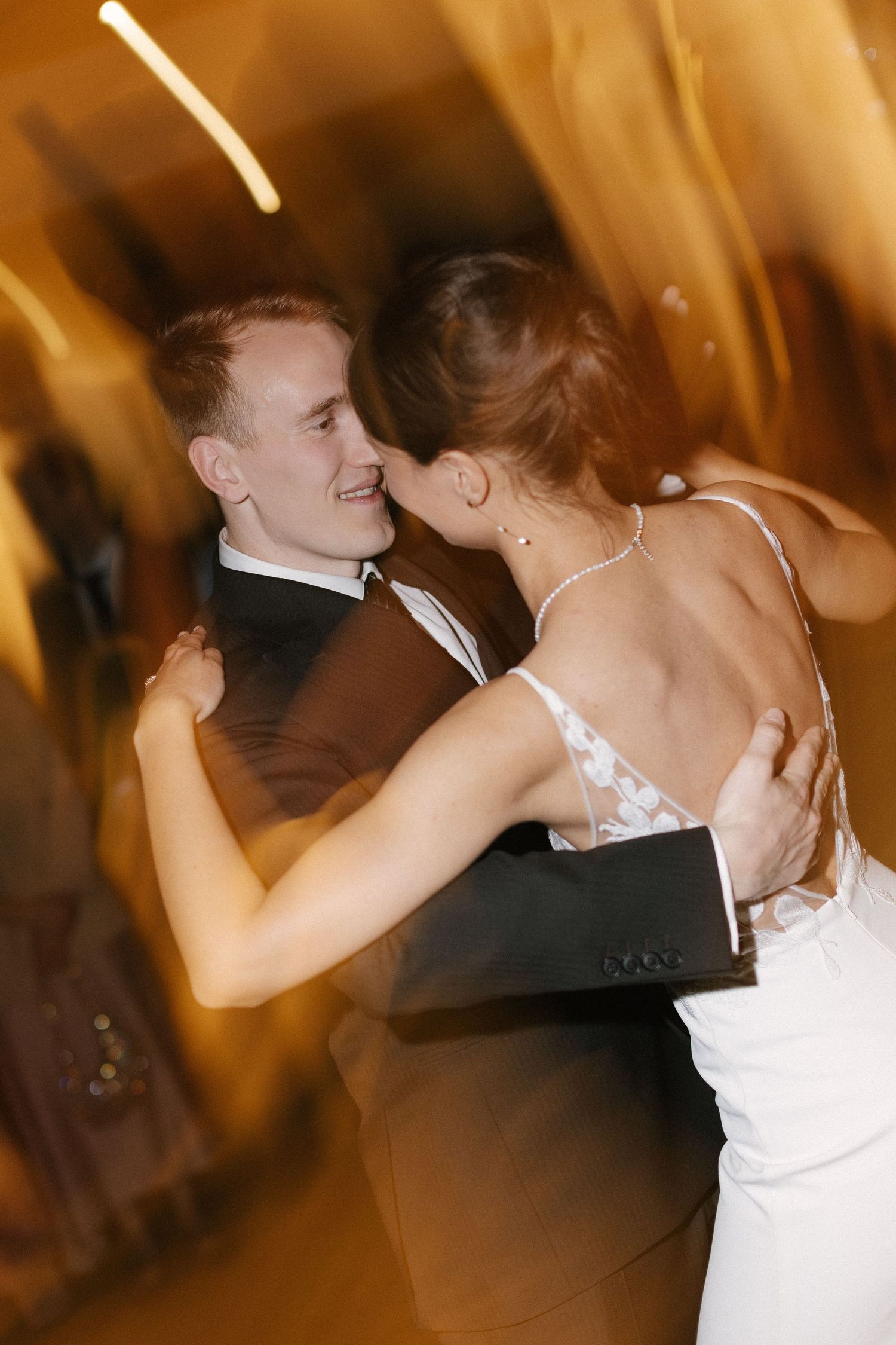 Bride and groom share an intimate first dance, smiling closely together in elegant wedding attire.